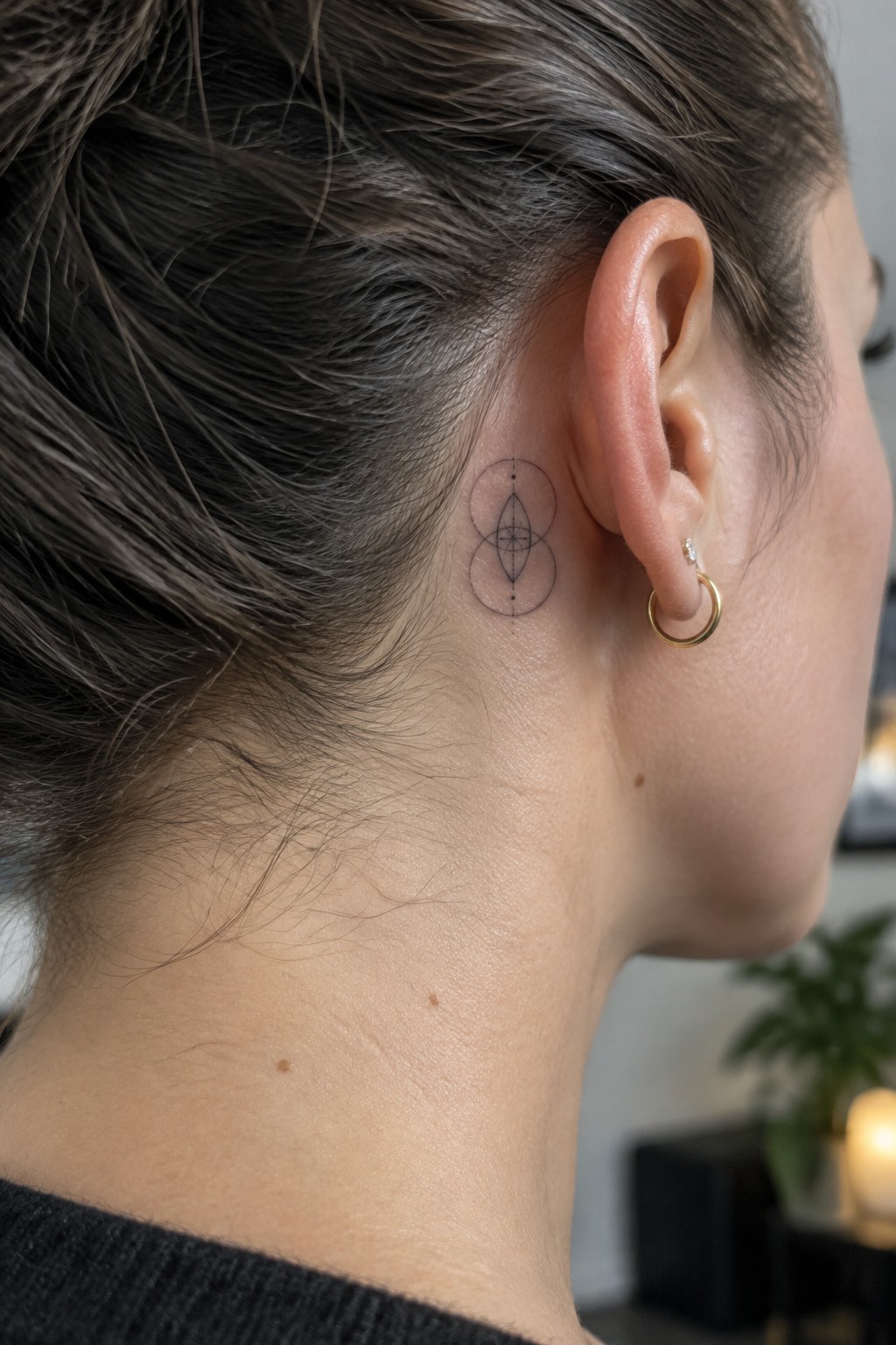 Woman's neck with geometric circle tattoo behind ear and gold hoop earring