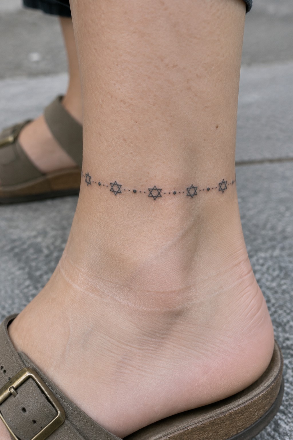 Ankle tattoo of Star of David symbols linked by dotted lines above brown sandal.