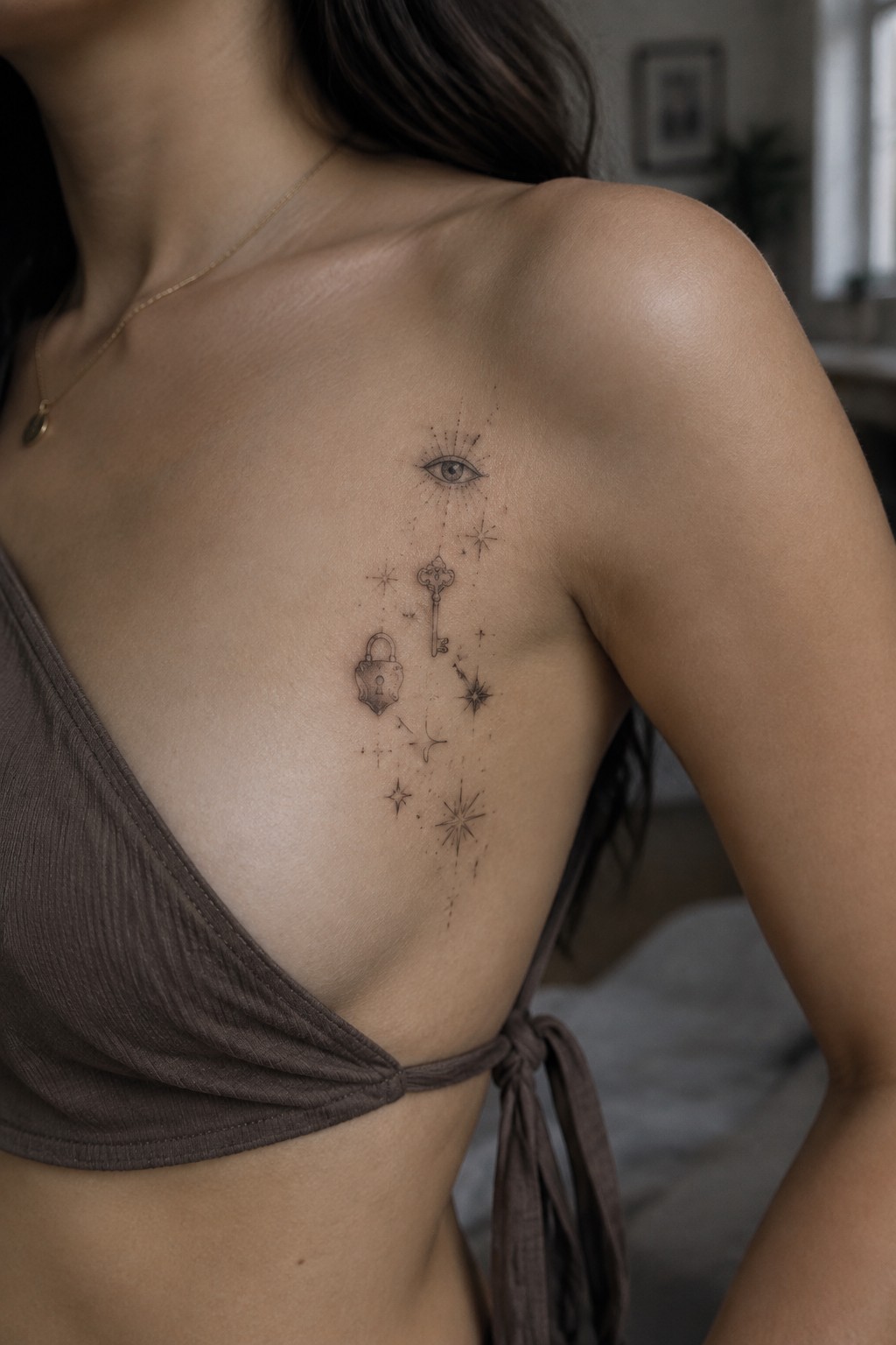 Shoulder tattoo of eye, key, padlock, and stars above brown top.