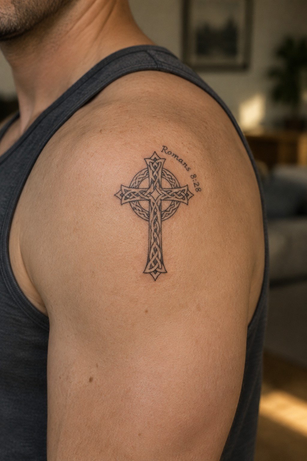 Man's shoulder in gray tank top with Celtic cross tattoo and Romans 8:28 text