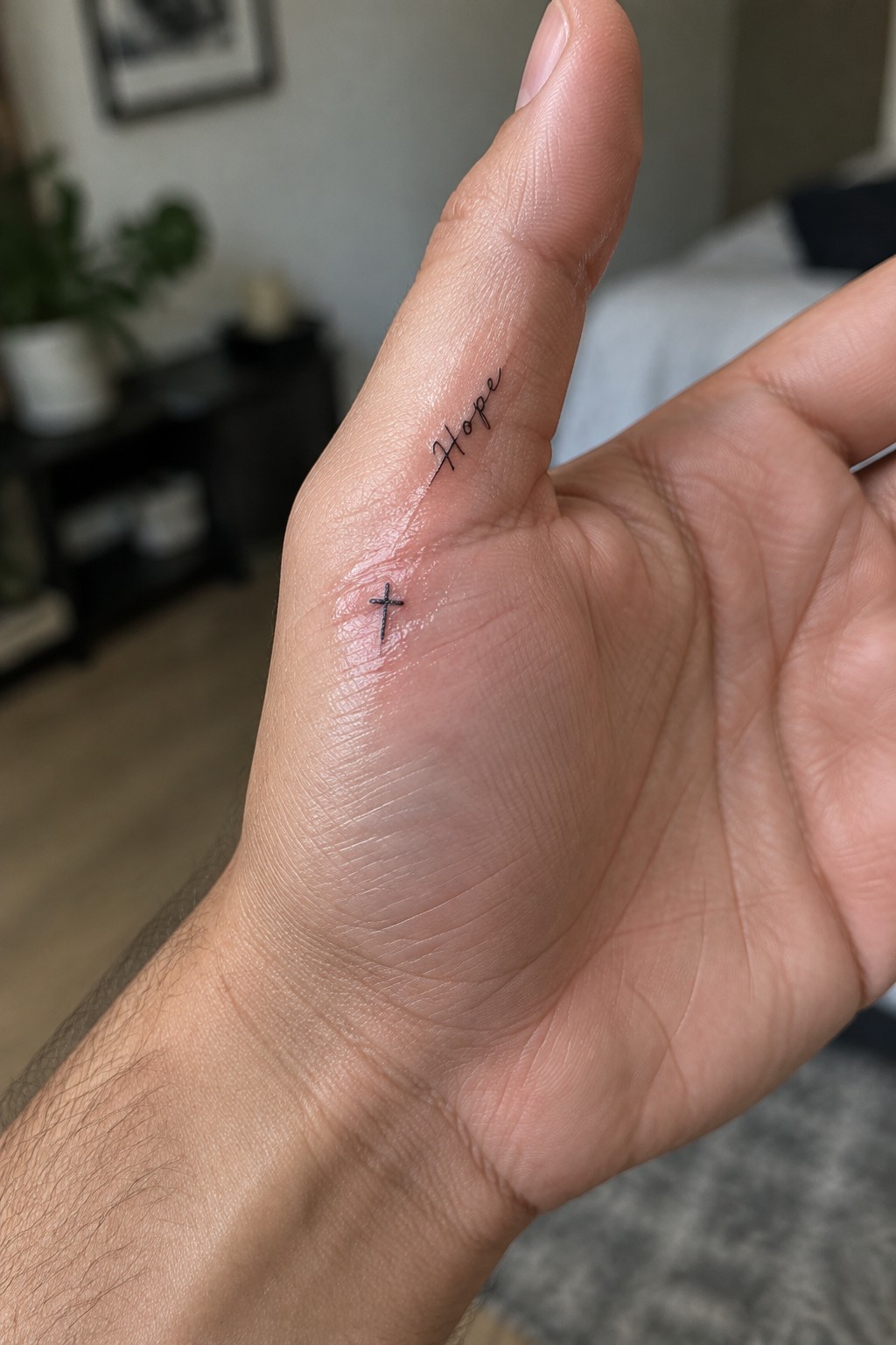 Hand with black cursive 'Hope' tattoo above small cross on skin