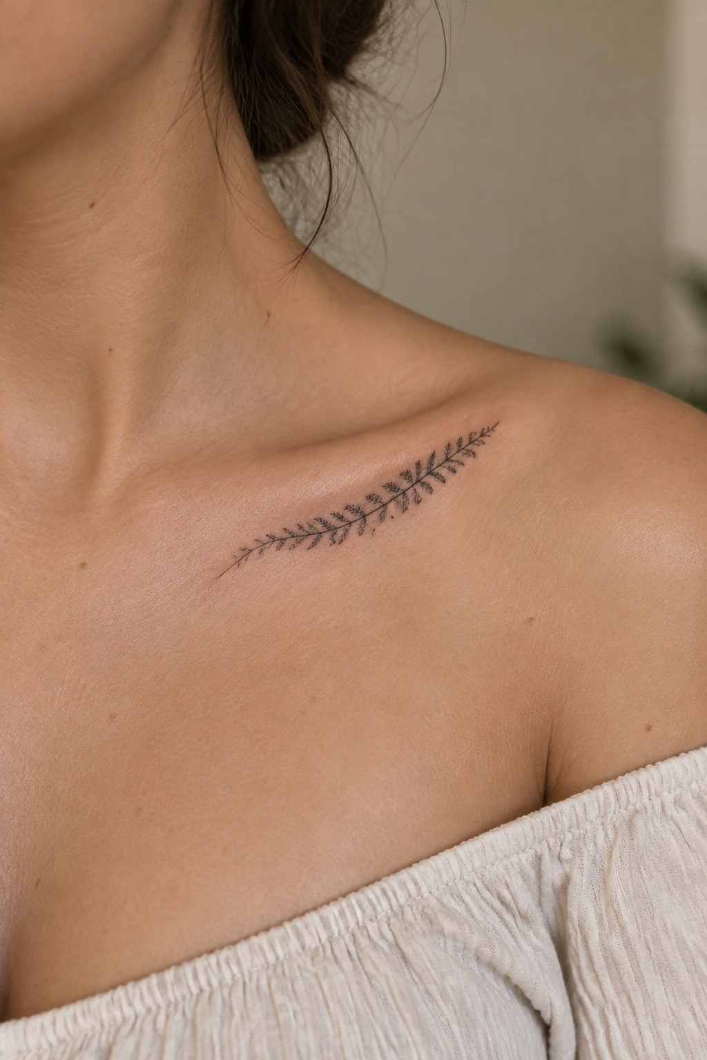 Delicate black fern tattoo on woman's shoulder above white off-shoulder top