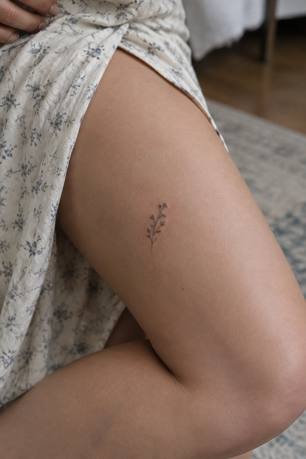 Small plant tattoo on thigh beneath light floral-patterned fabric skirt
