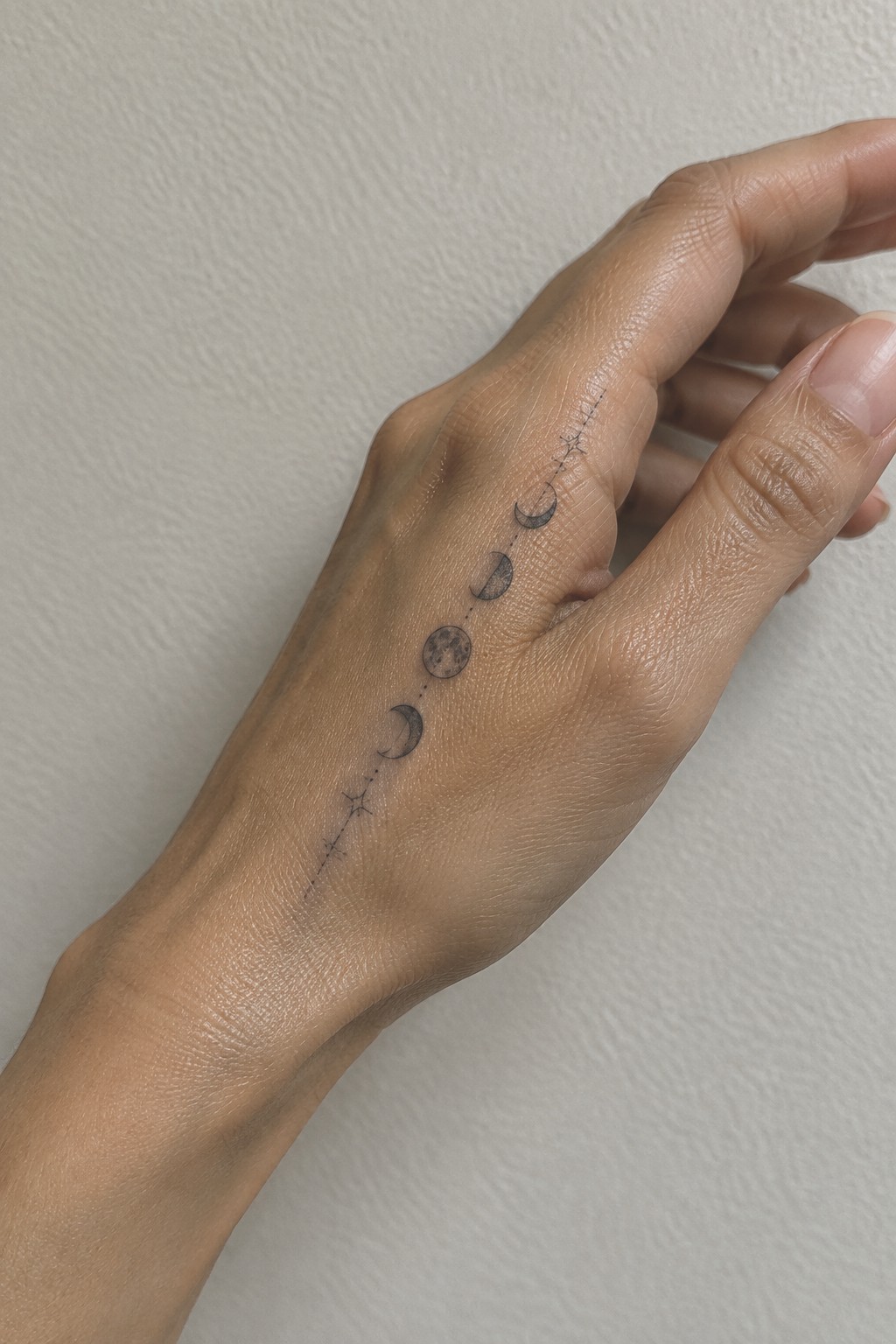 Hand with moon phases tattoo connected by dotted lines and stars.
