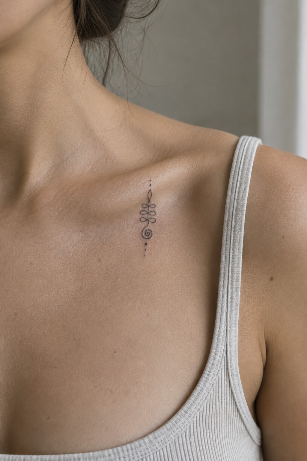 Woman's collarbone with delicate black spiral and floral tattoo above white tank top