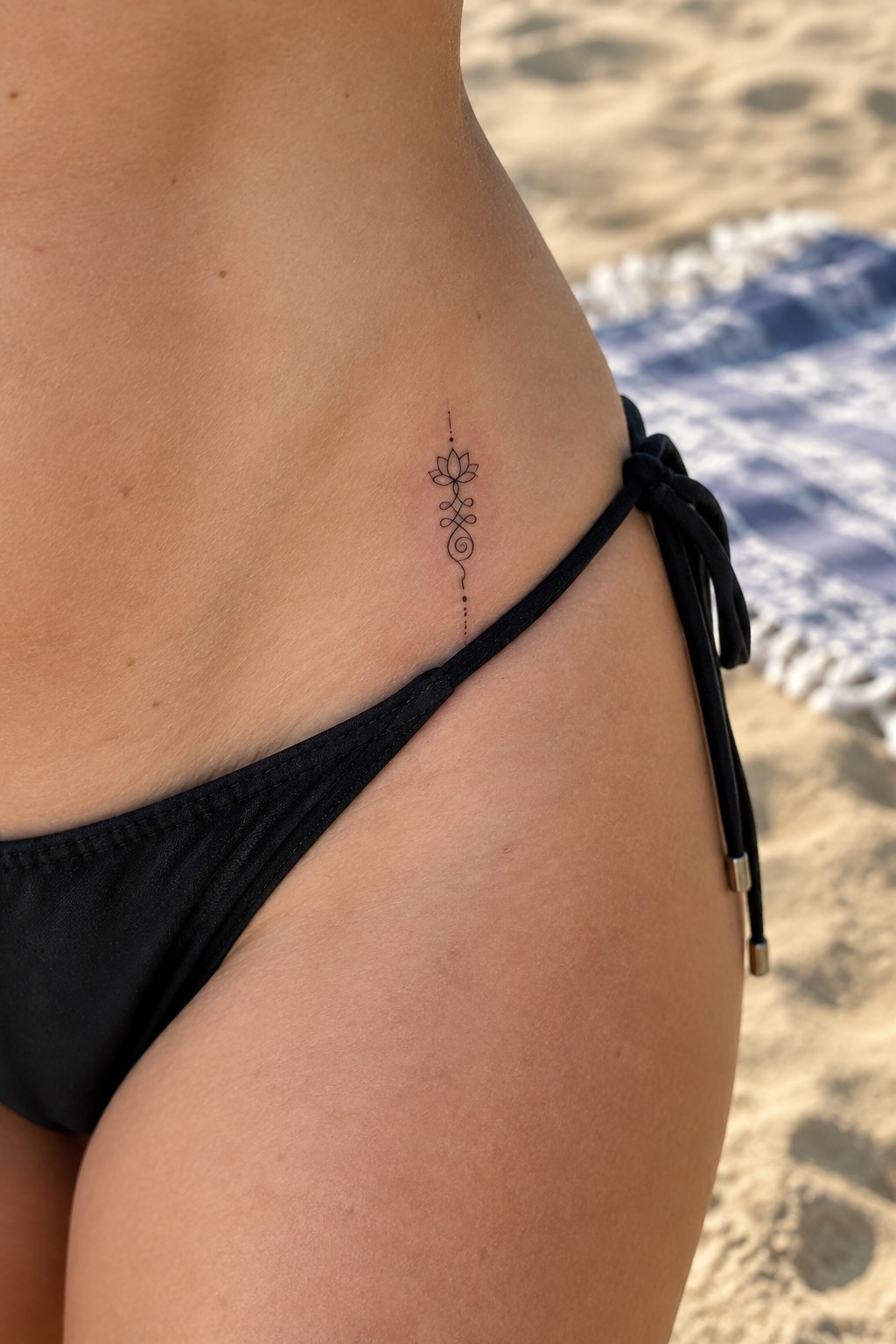 Lotus flower tattoo on hip above black bikini bottom at beach