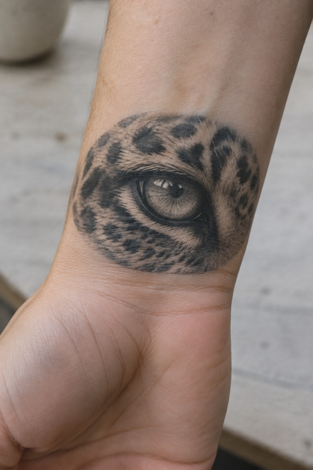 Detailed black-and-gray leopard-eye tattoo on a person's inner wrist