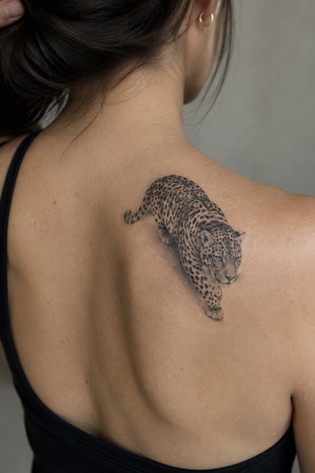 Realistic black and gray jaguar tattoo on a woman's upper back in a prowling pose.