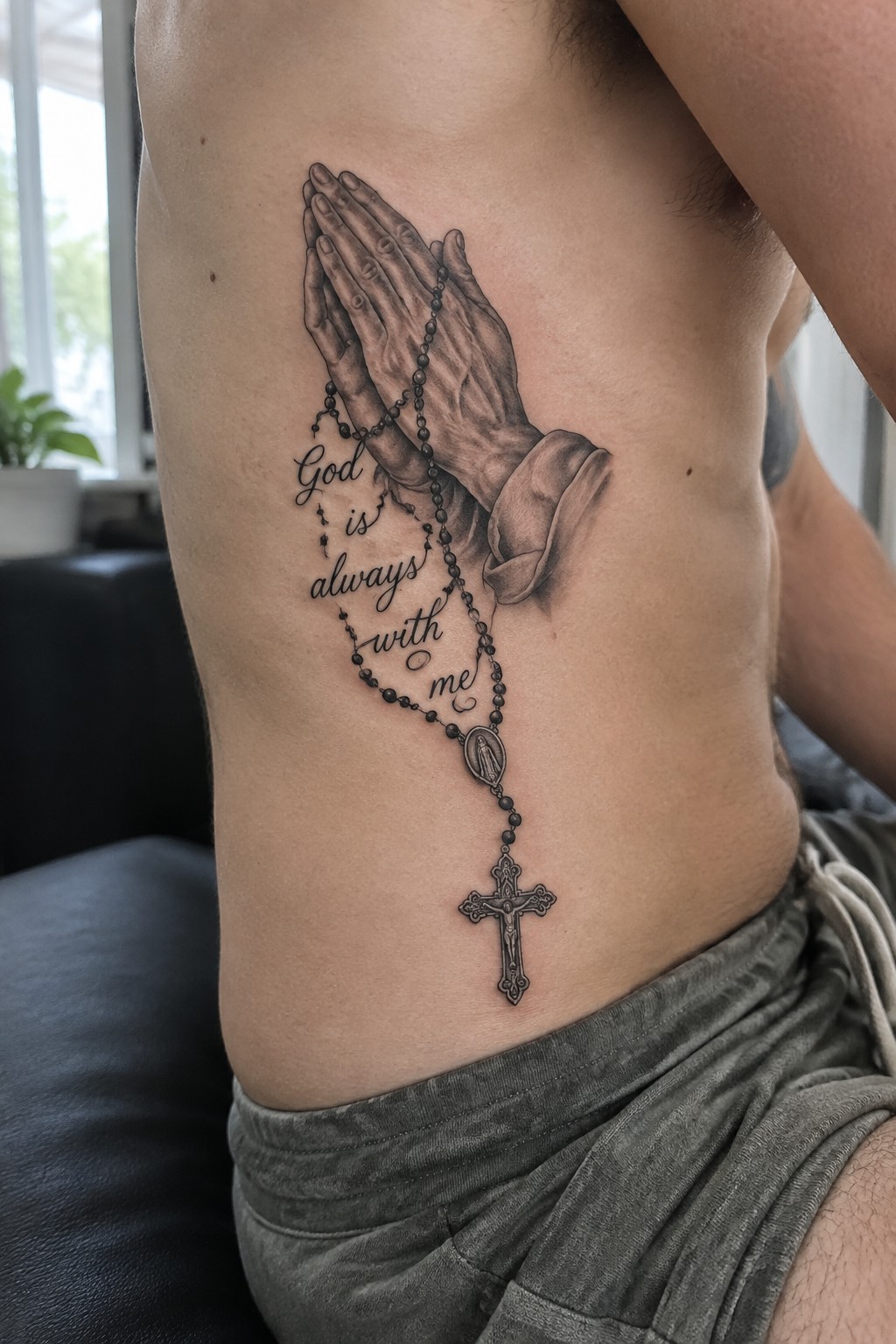 Black and gray tattoo of praying hands with rosary and cross on torso.