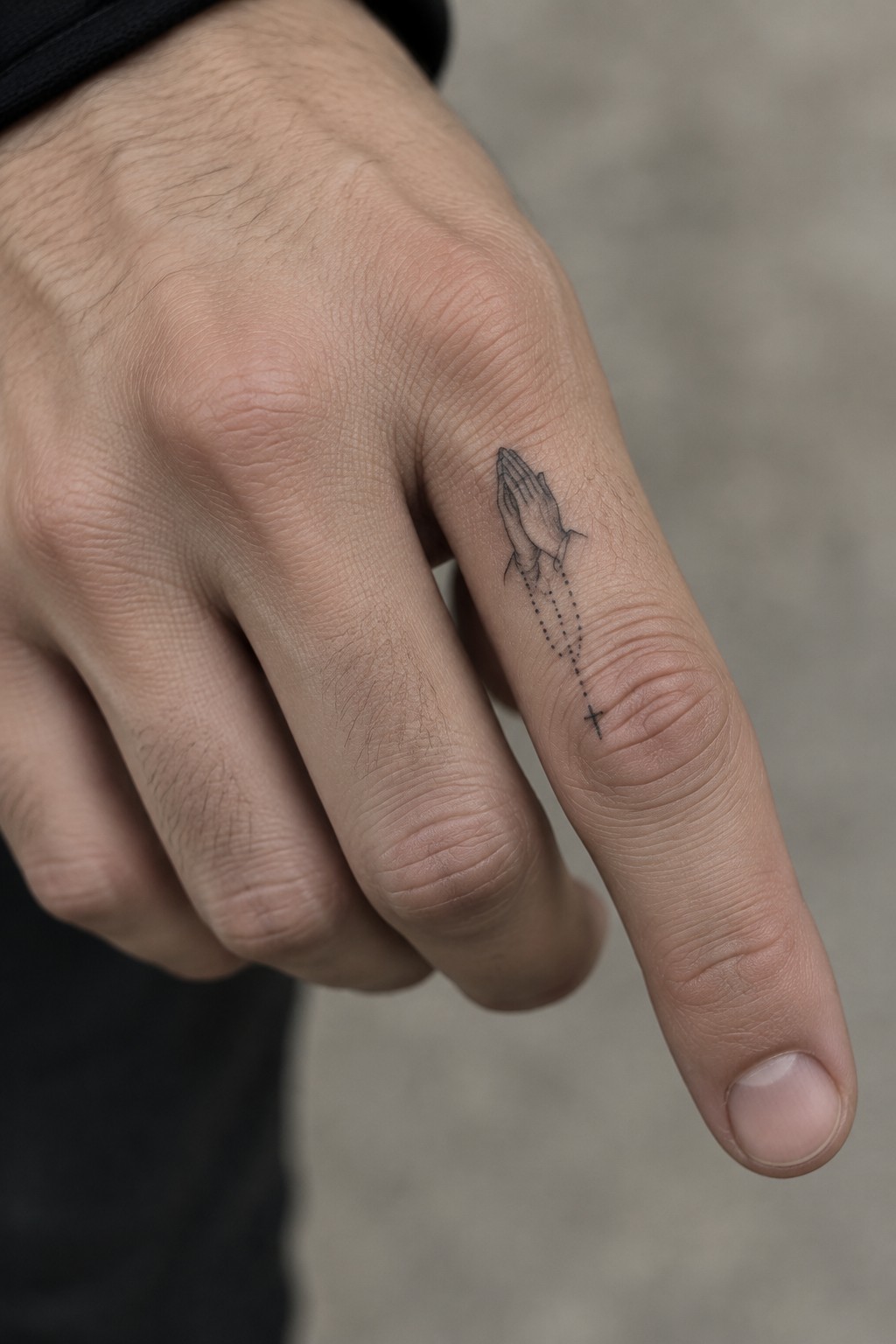 Close-up of light-skinned hand with black praying hands rosary tattoo on finger.