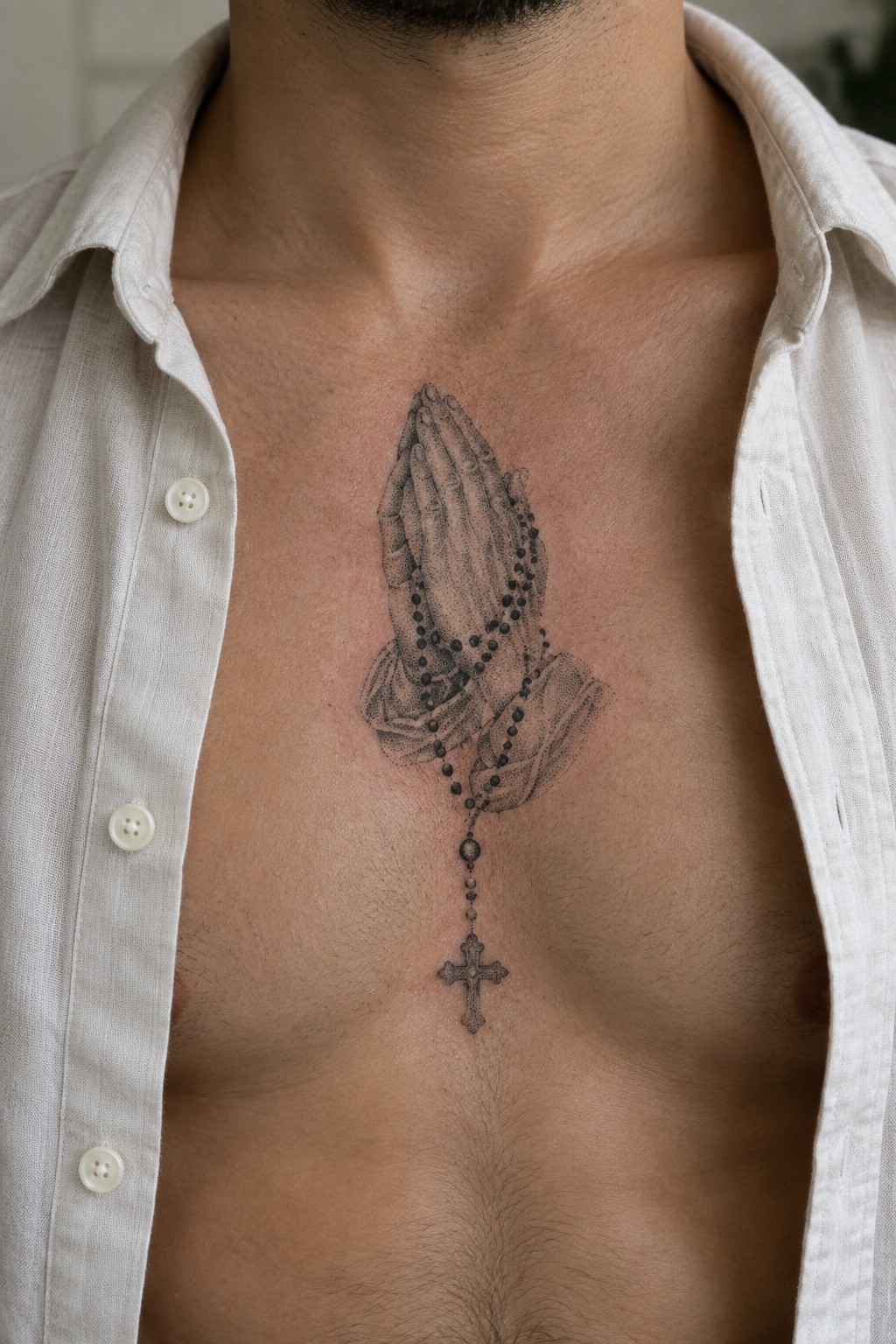 Open white shirt revealing detailed praying hands rosary tattoo on man's chest