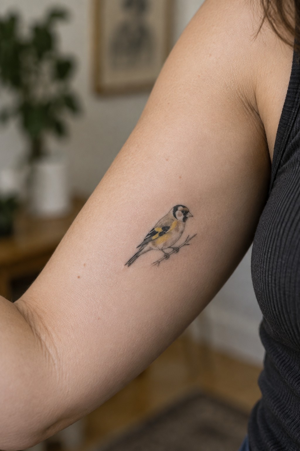 Realistic goldfinch tattoo on upper arm of person in dark gray tank top
