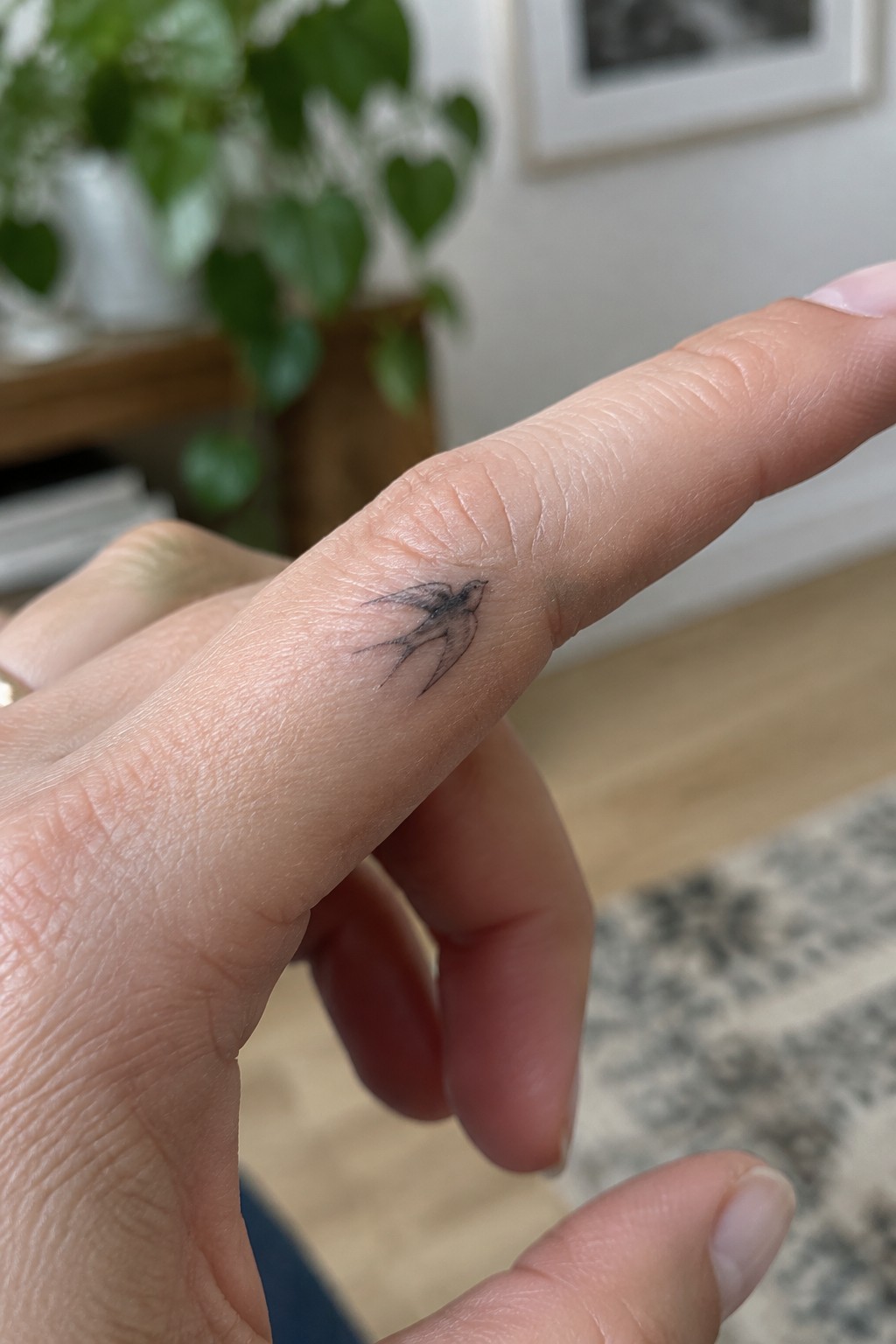 Close-up of index finger with small black swallow tattoo near knuckle.