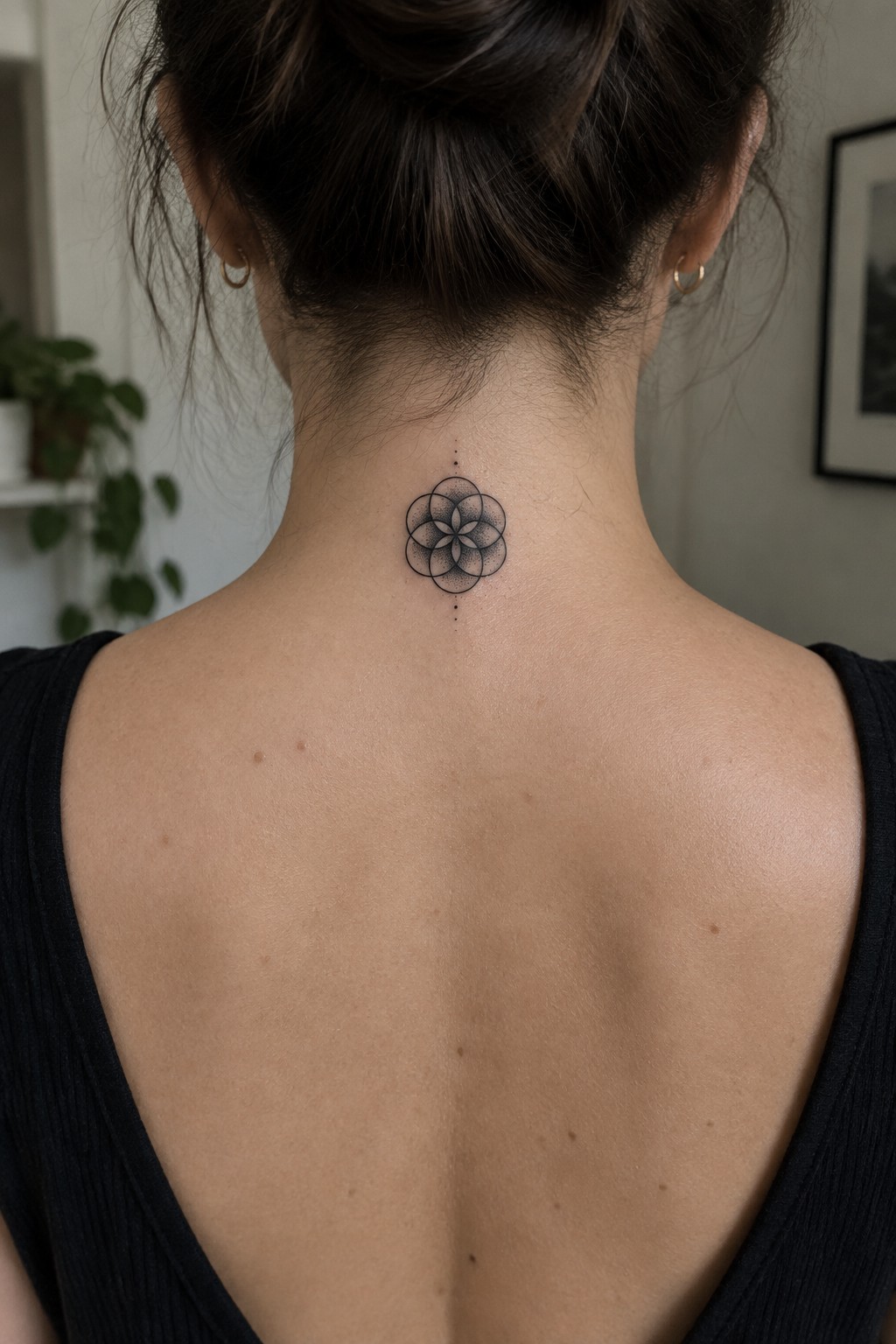 Woman's neck with geometric flower tattoo, dark bun, black low-back top