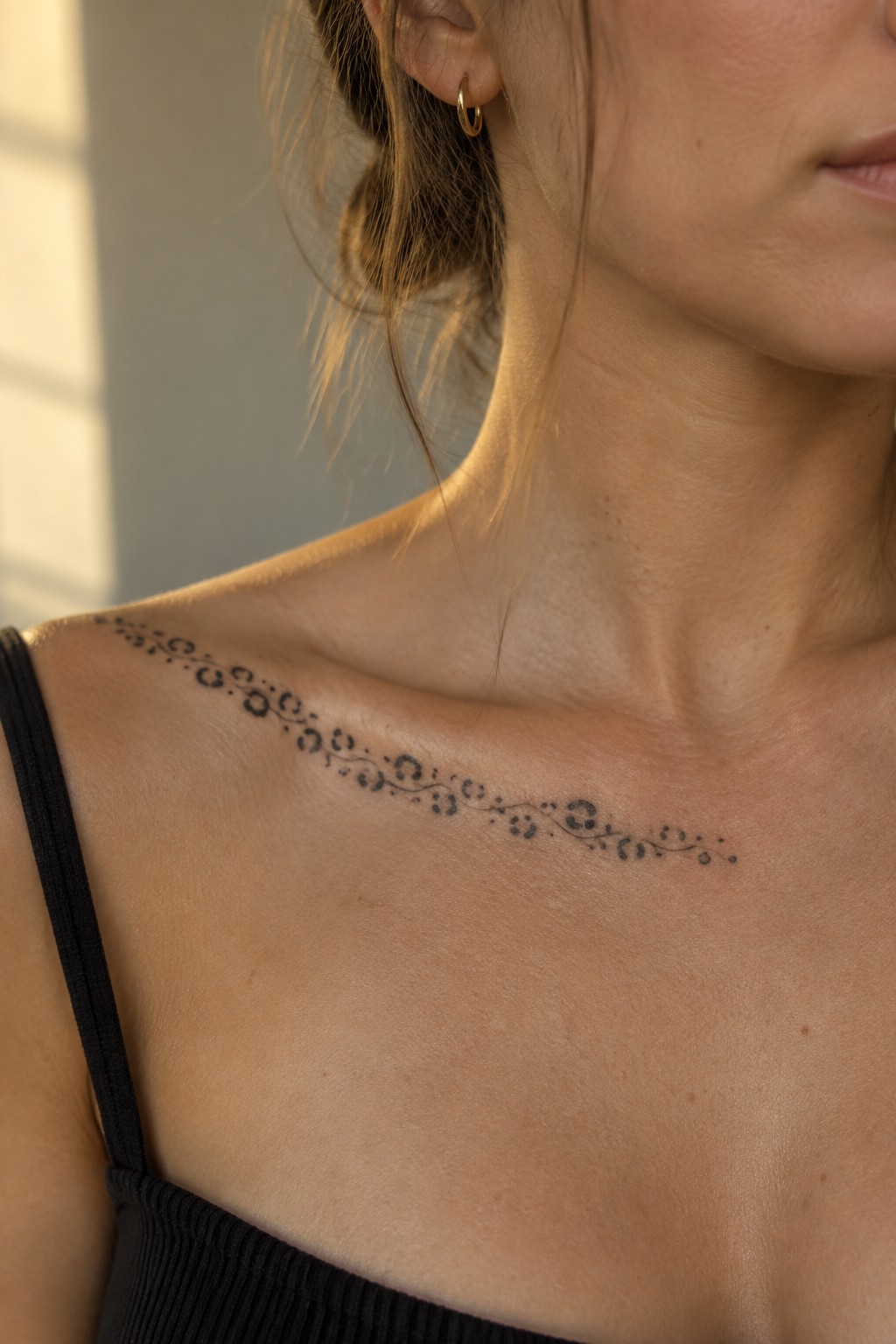 Fine line tattoo with spotted circles and thin swirls across a woman's collarbone in natural light