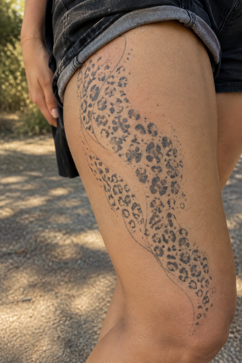 Leopard print tattoo curving along thigh below rolled-up denim shorts