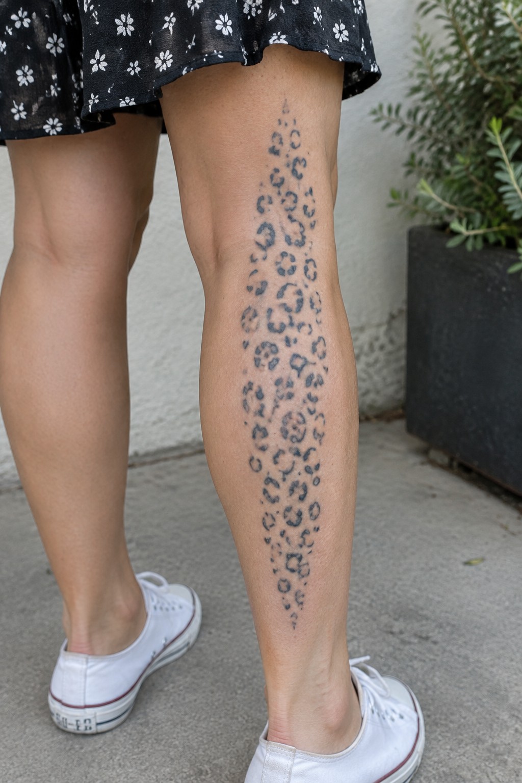 Leopard print tattoo on leg under black floral skirt with white sneakers.