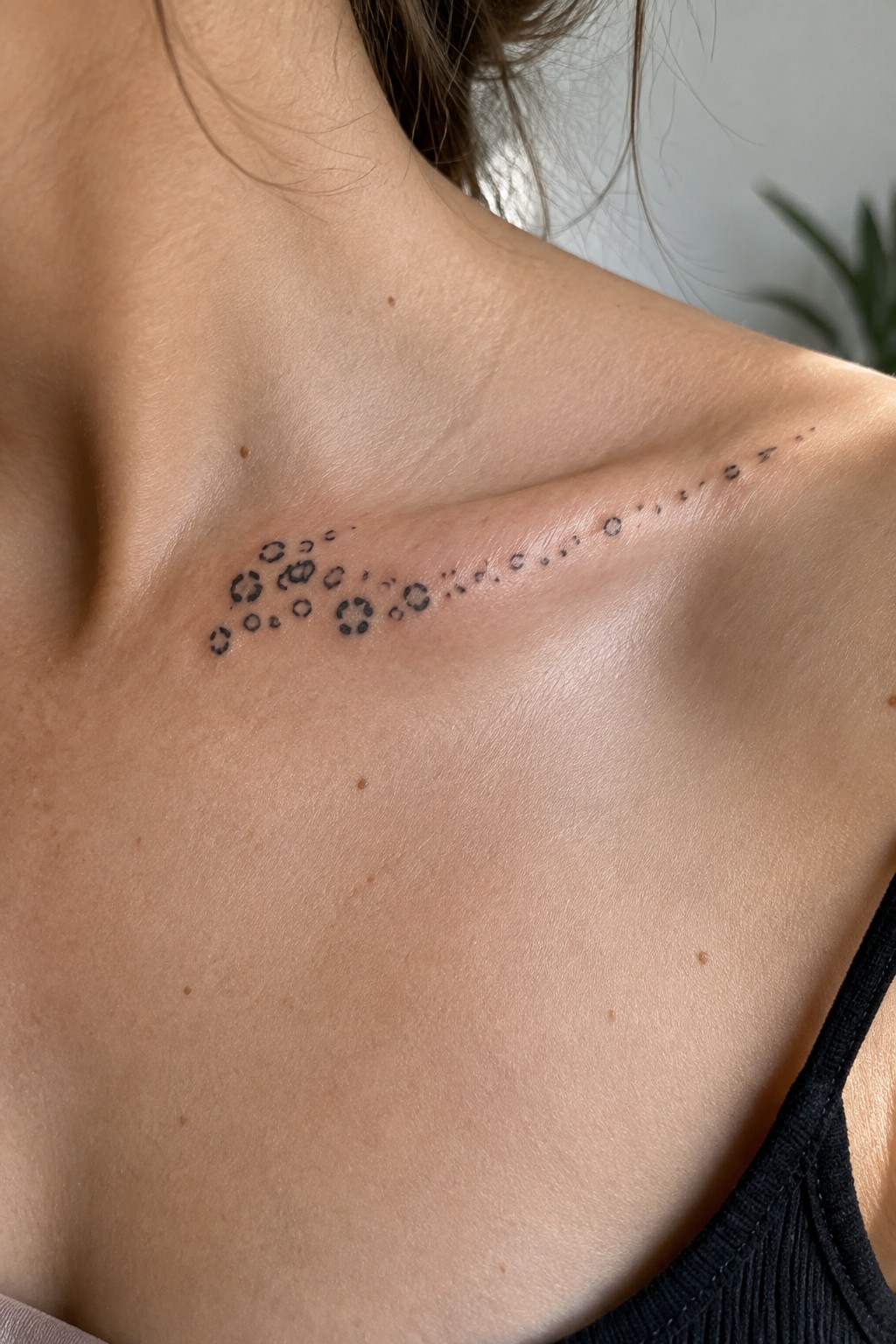 Abstract circular tattoo design curving across light skin on shoulder and collarbone.