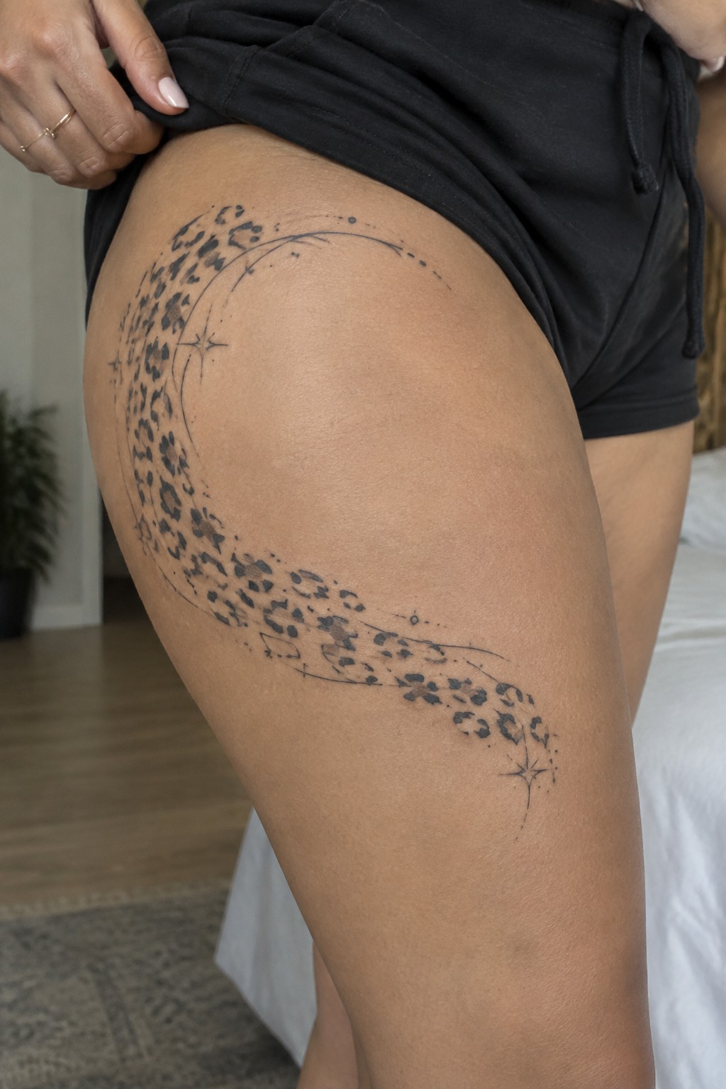 Leopard-print crescent moon tattoo on thigh under lifted black shorts with rings
