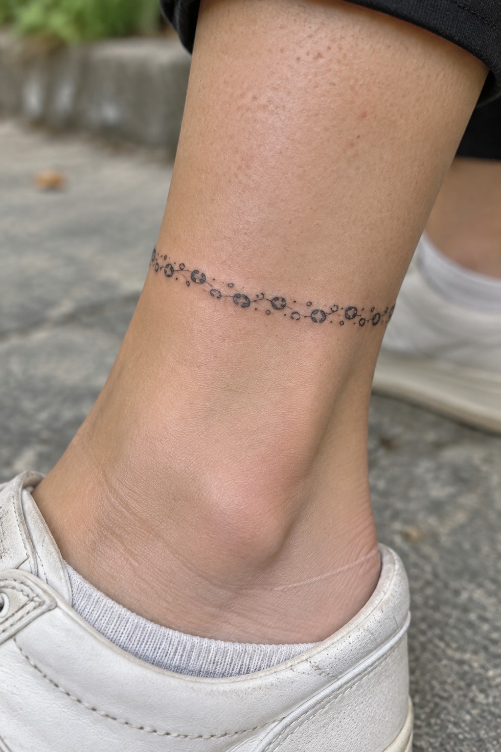 Light-skinned ankle with black connected-dot tattoo above white sneaker and sock