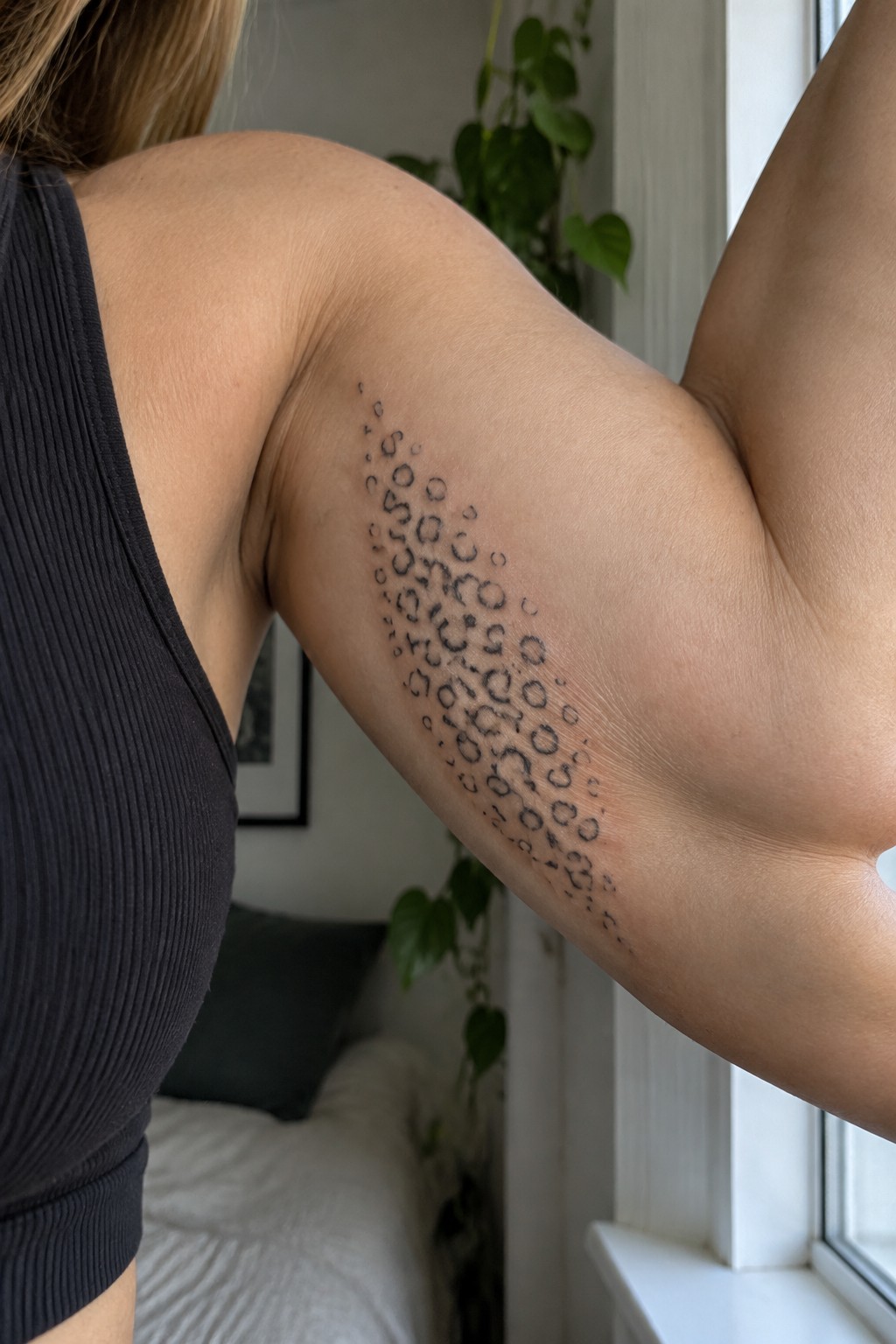 Fine line black ink leopard print tattoo on a woman's upper arm showing a vertical arrangement of open circles and spots.