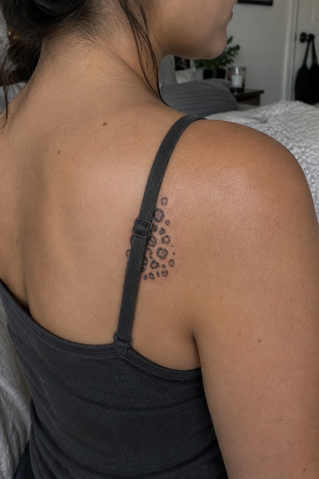Woman's upper back with leopard spot tattoo under gray tank top strap