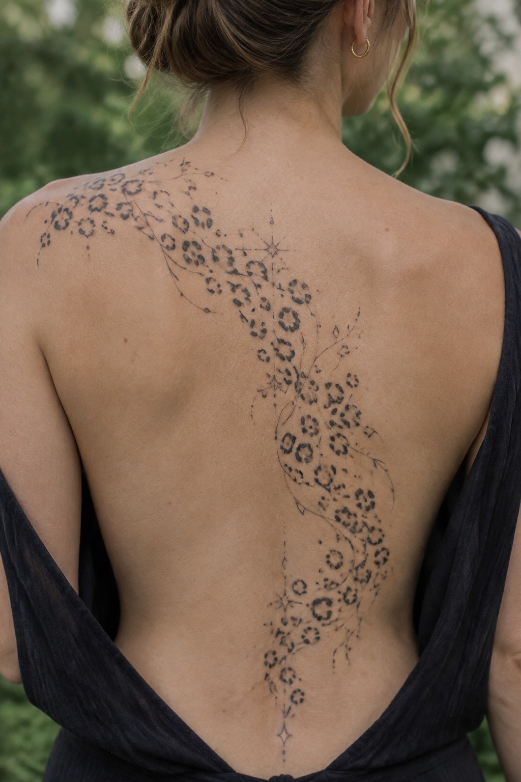 Woman's back with intricate floral star tattoo under dark open-back top.
