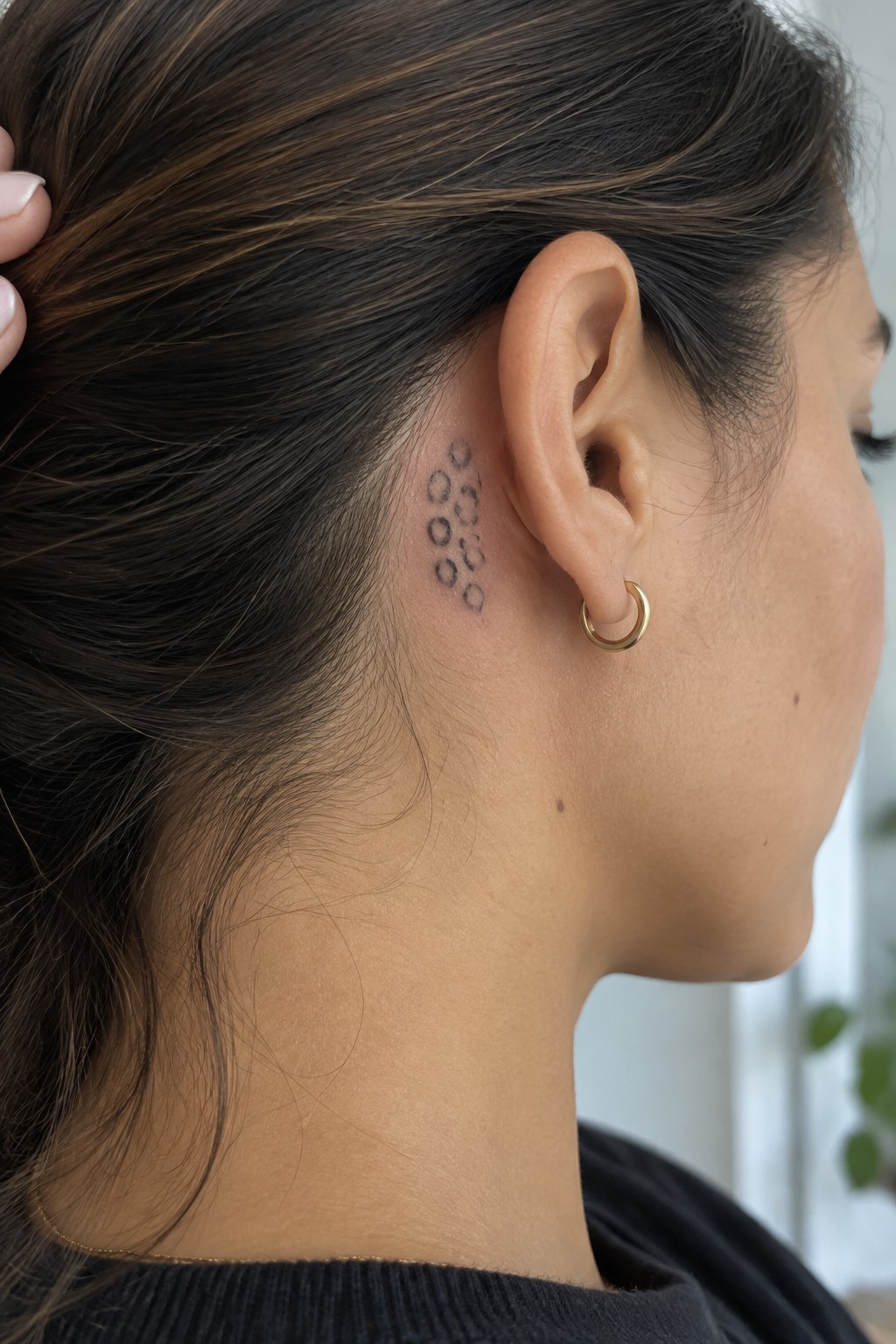 Woman with brown hair, circular neck tattoo, gold hoop earring, and thin necklace