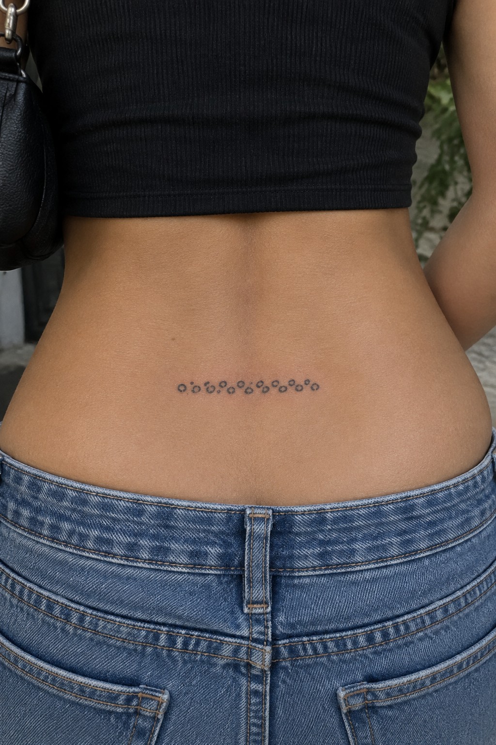 Lower back with dotted tattoo above blue jeans and black crop top