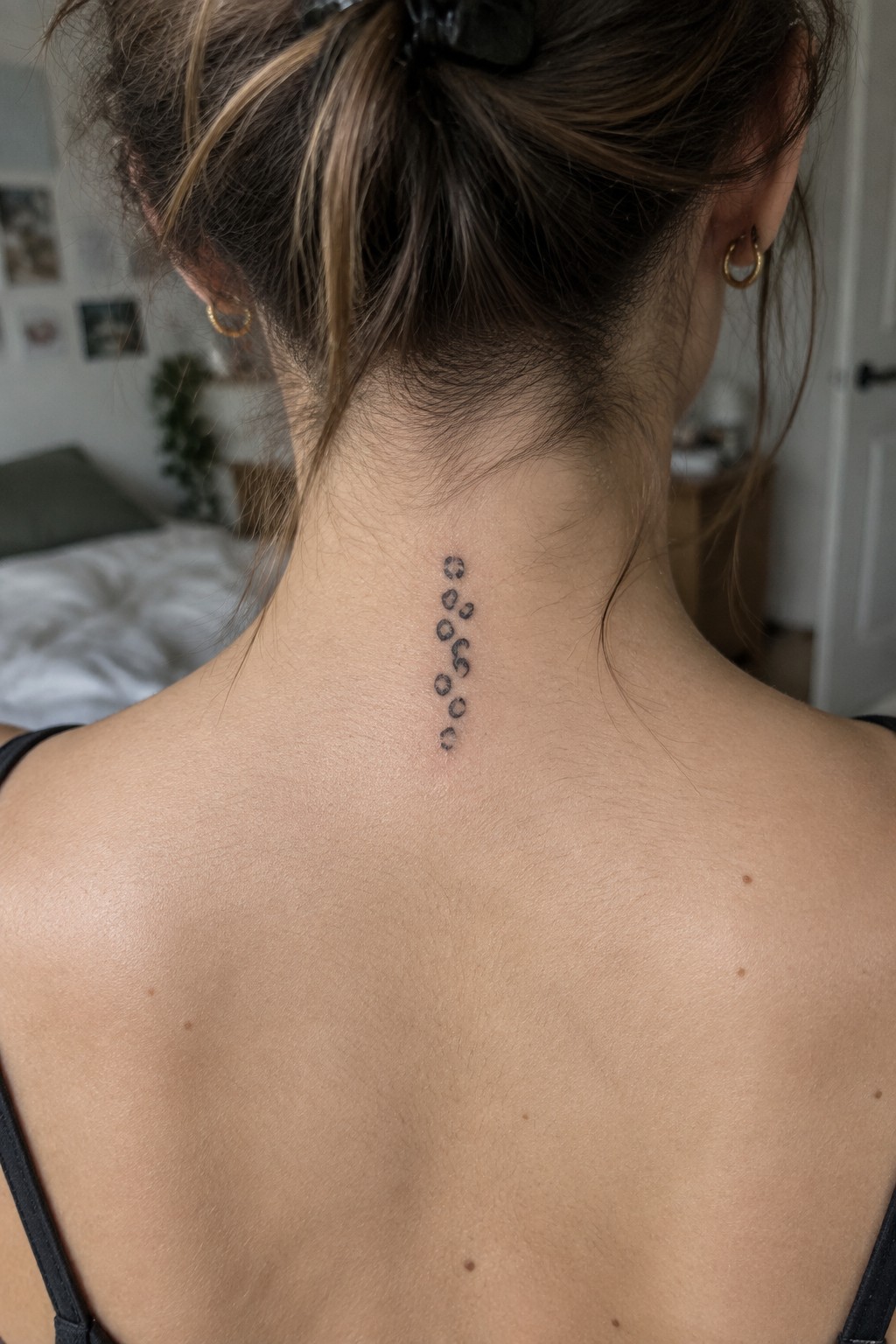 Fine line leopard spot tattoo arranged vertically down the back of a woman's neck