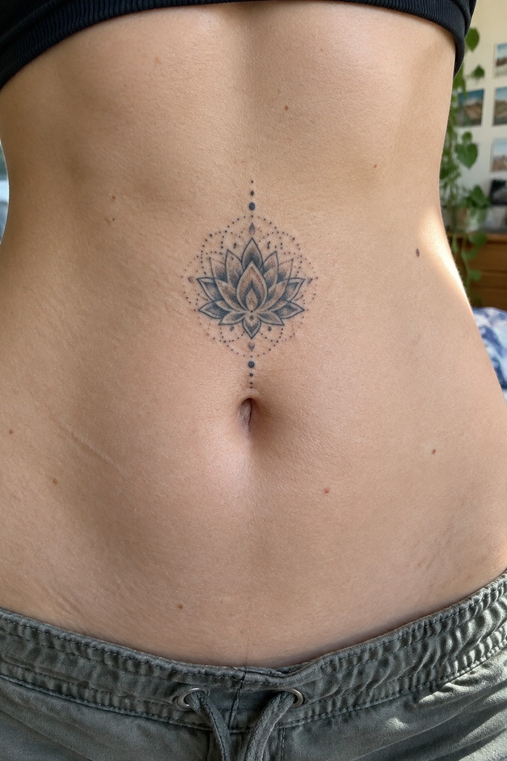 Lotus tattoo on midriff above navel, black top and gray pants visible