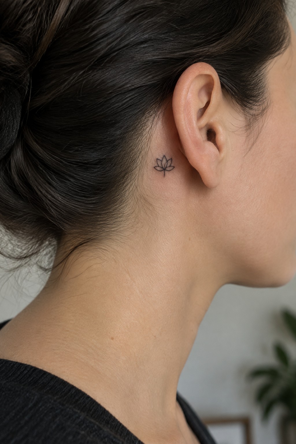 Dark hair in bun with small lotus tattoo behind ear on neck.