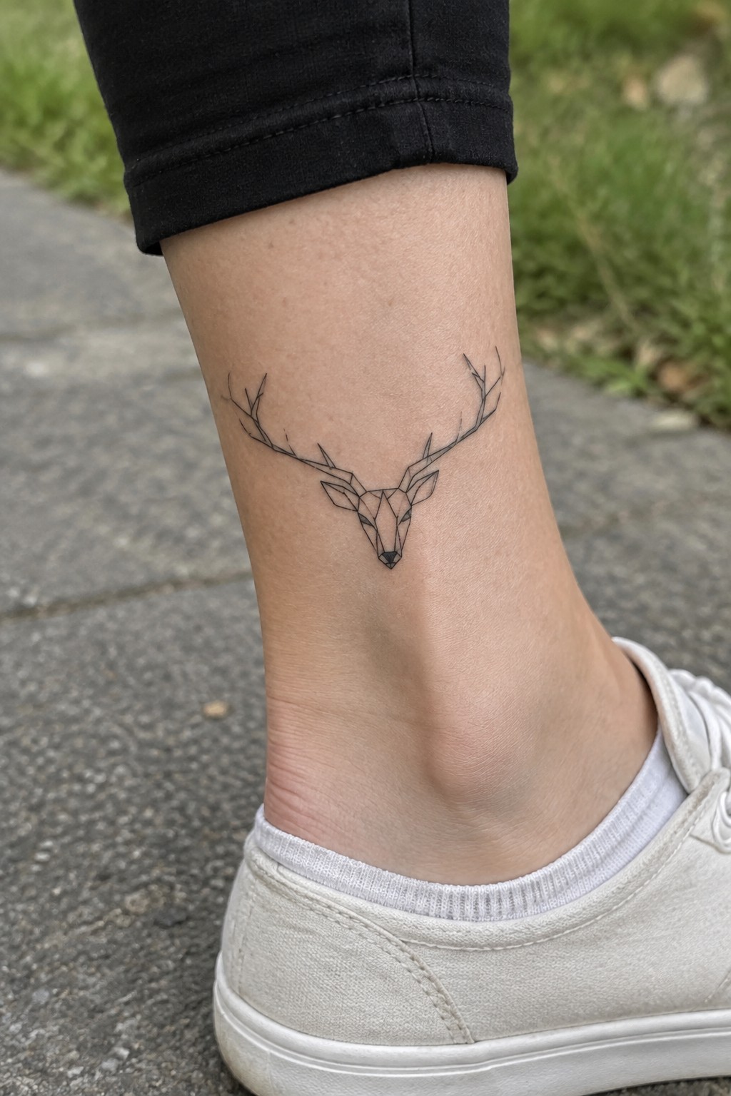 Geometric deer head tattoo on ankle above white sneaker and black pants cuff.