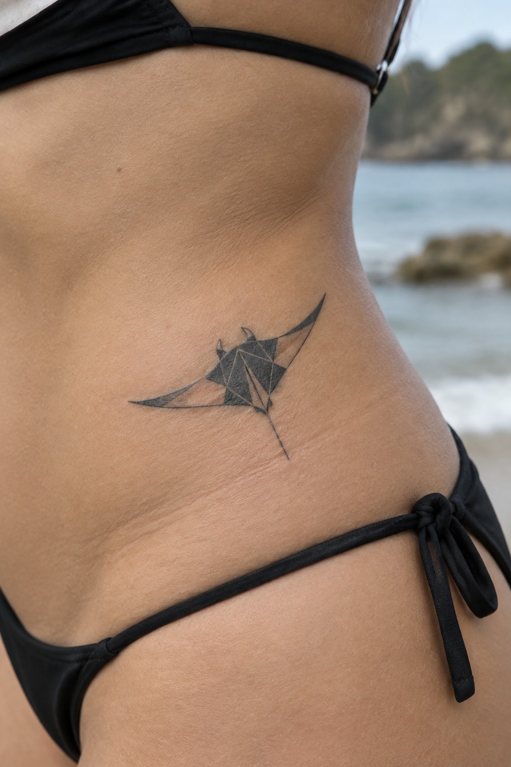 Woman's side with black bikini and geometric manta ray tattoo by ocean