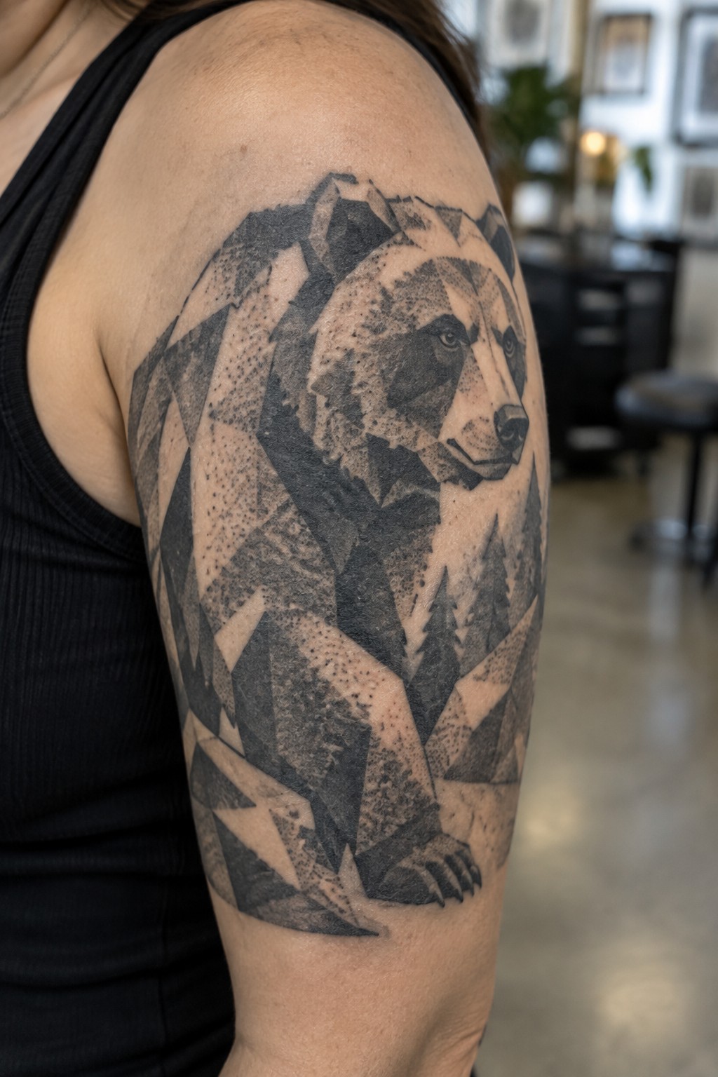 Geometric black-and-gray bear tattoo on arm of person in black tank top.