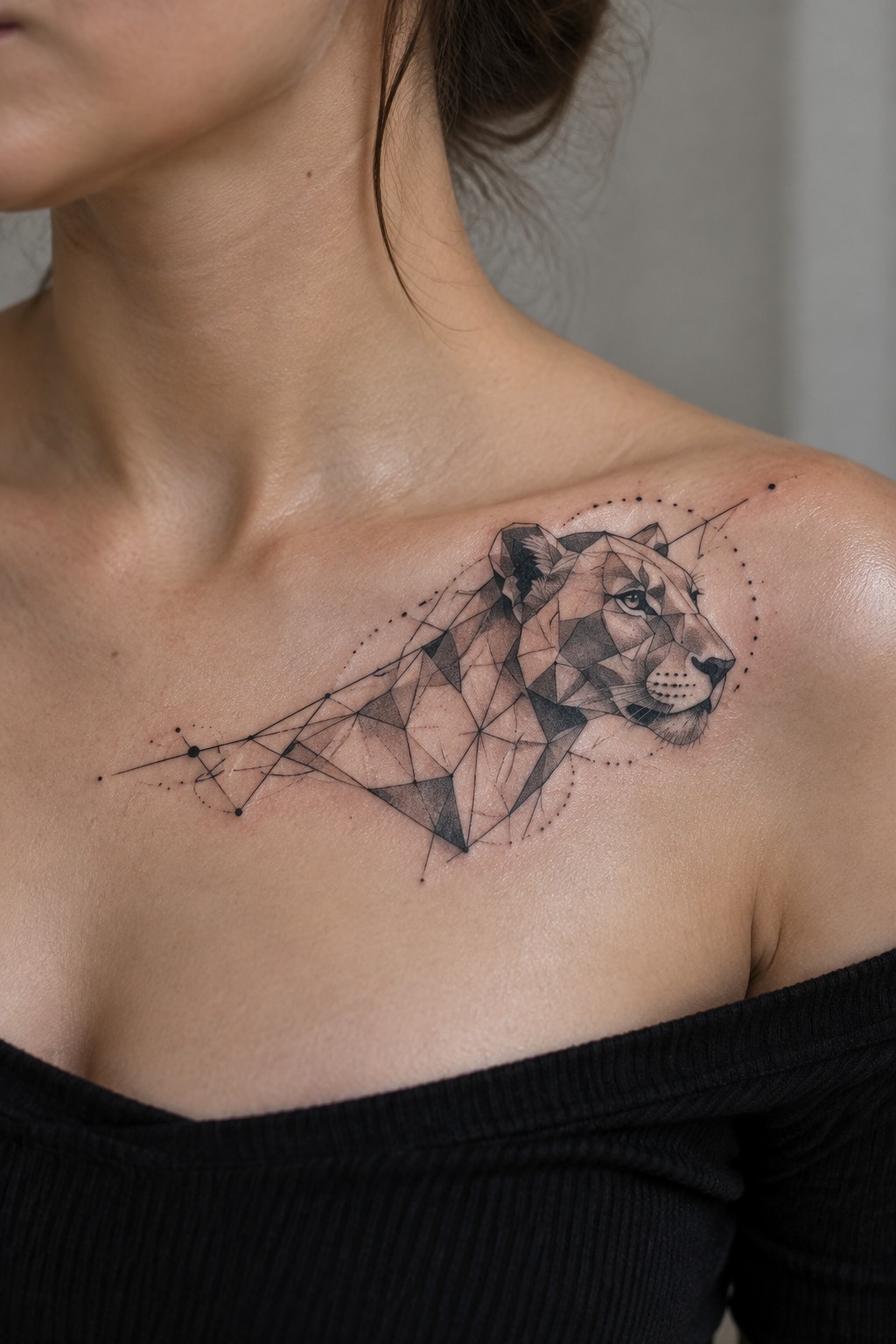 Geometric lion tattoo on woman's shoulder above black off-shoulder top