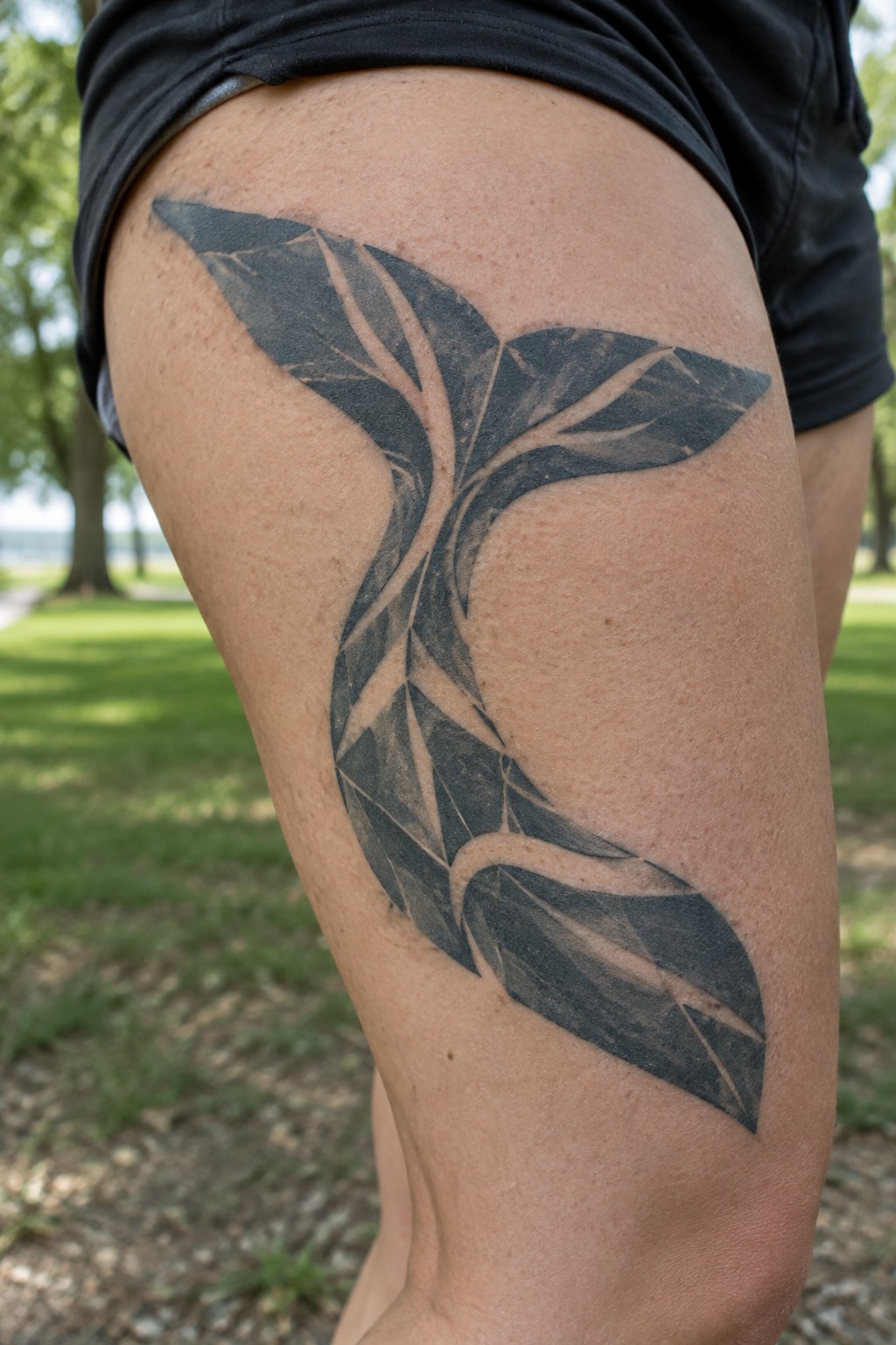 Geometric black tattoo with cracked patterns on thigh, black shorts, outdoor grass background