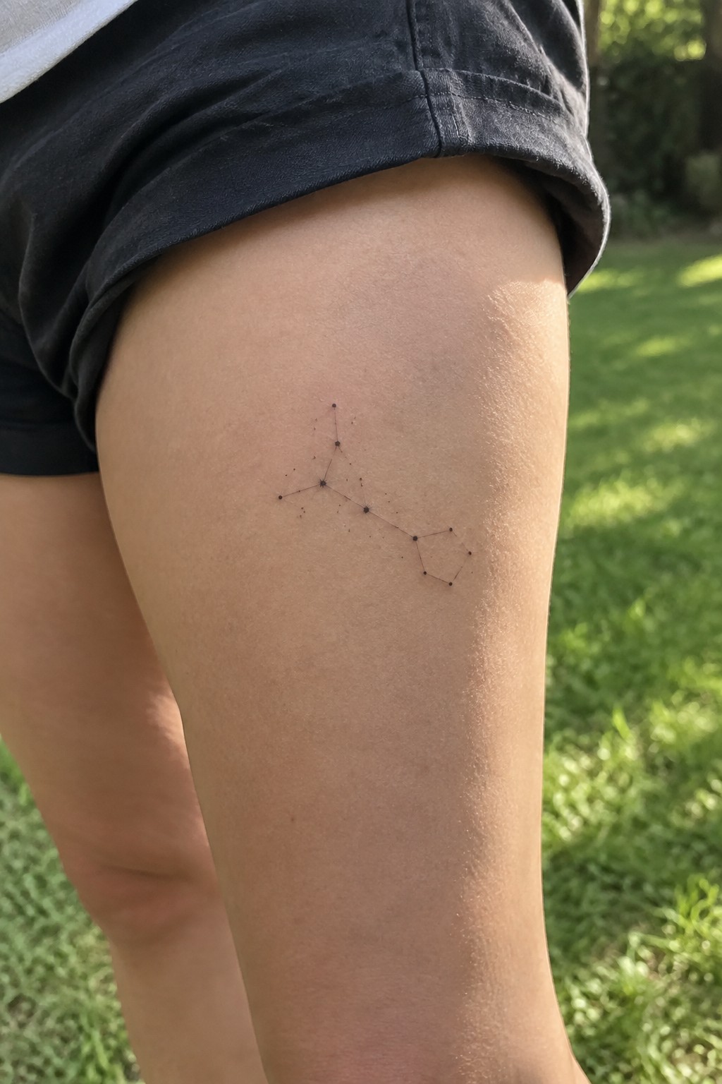 Black constellation tattoo on thigh with black shorts over green grass