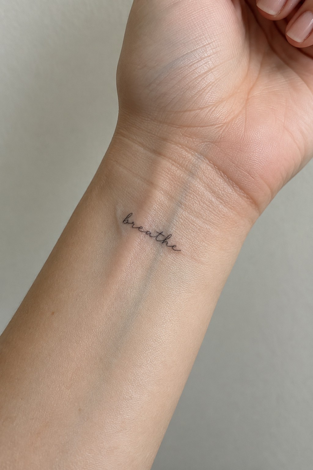 Pale wrist with delicate black cursive tattoo spelling 