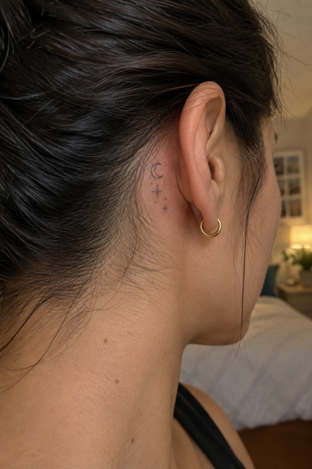 Fine line tattoo of a crescent moon and stars placed behind a woman's ear