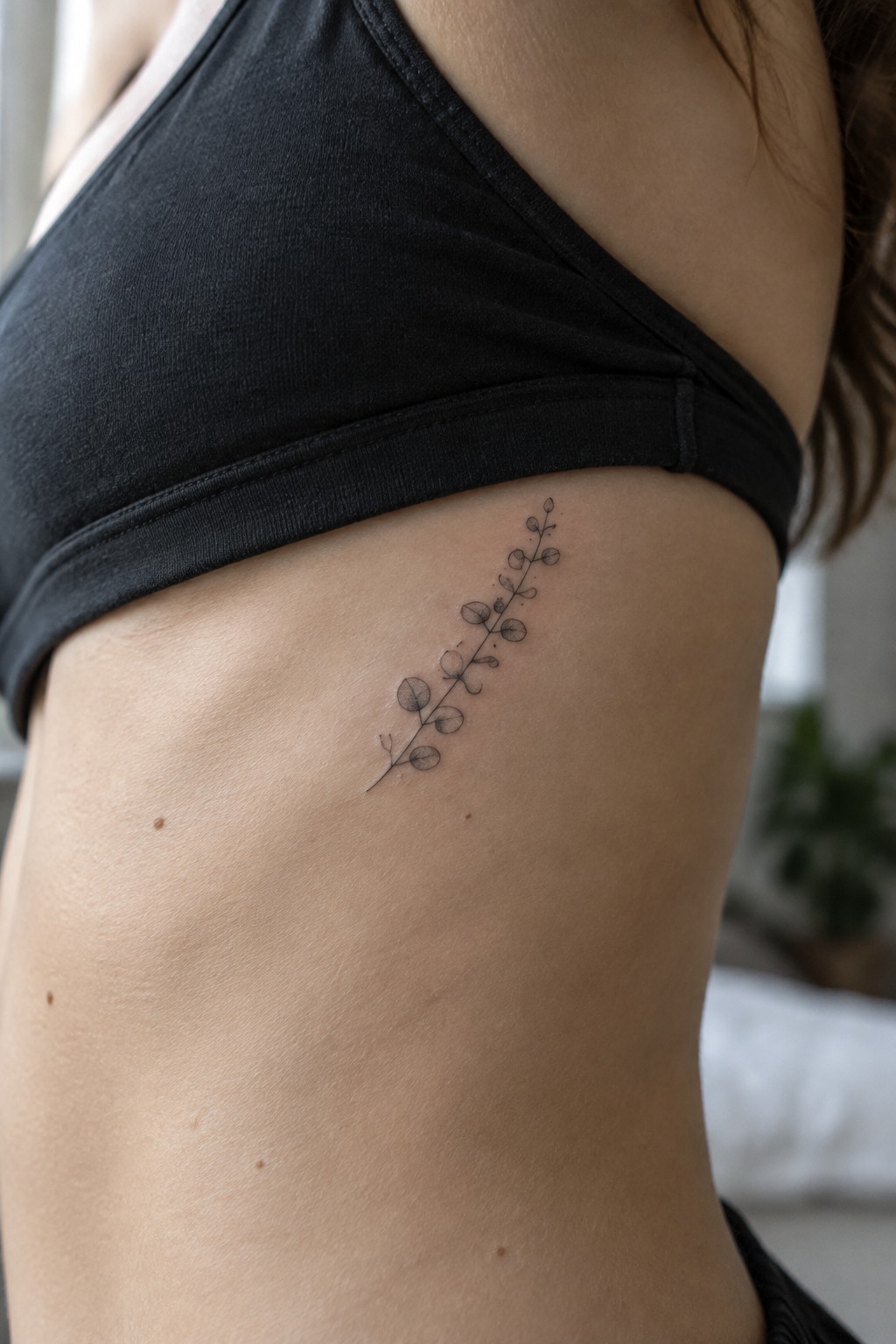 Fine line tattoo of a small leafy branch placed vertically on the ribs.