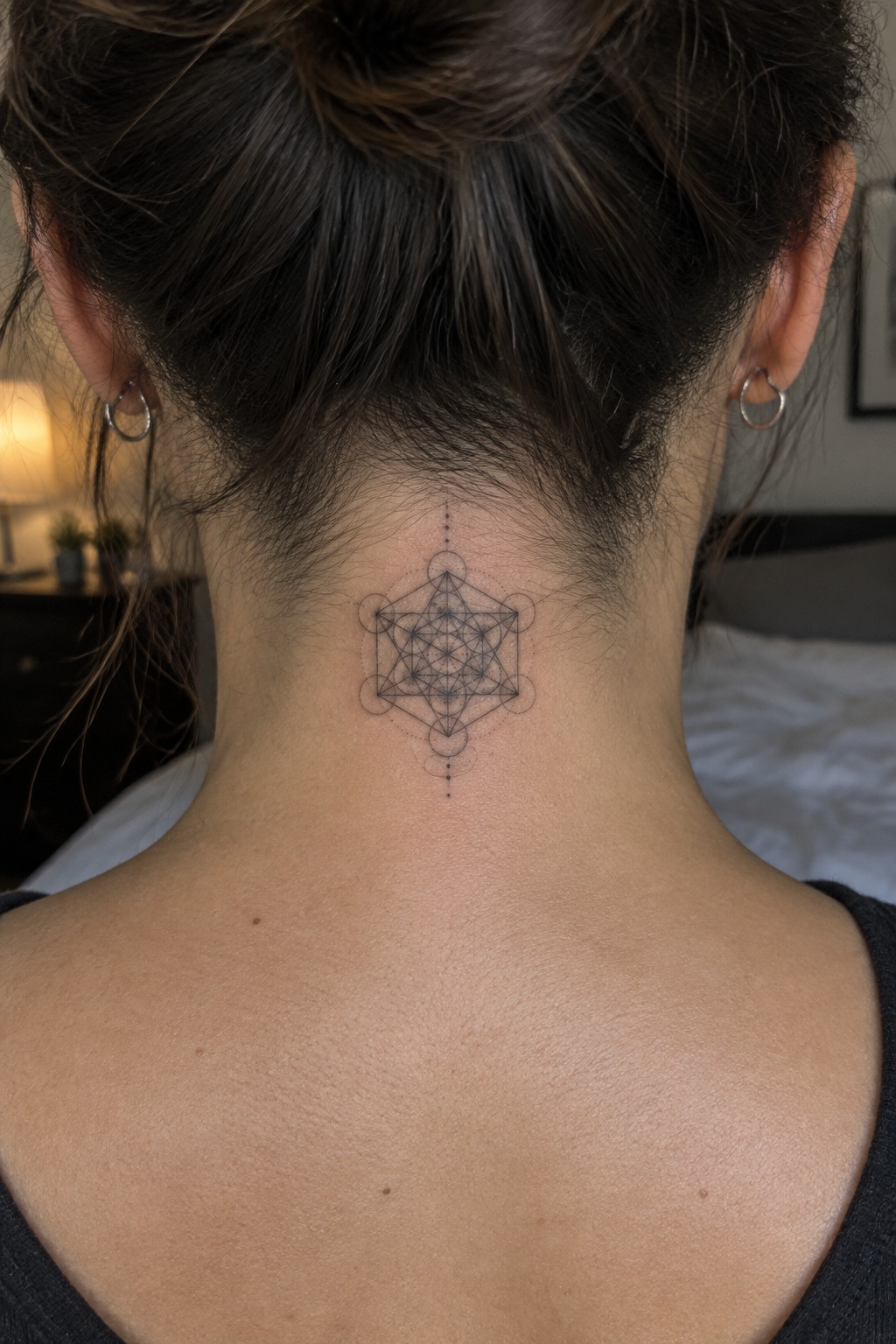 Back view of neck with intricate geometric tattoo, dark hair in bun, hoop earrings