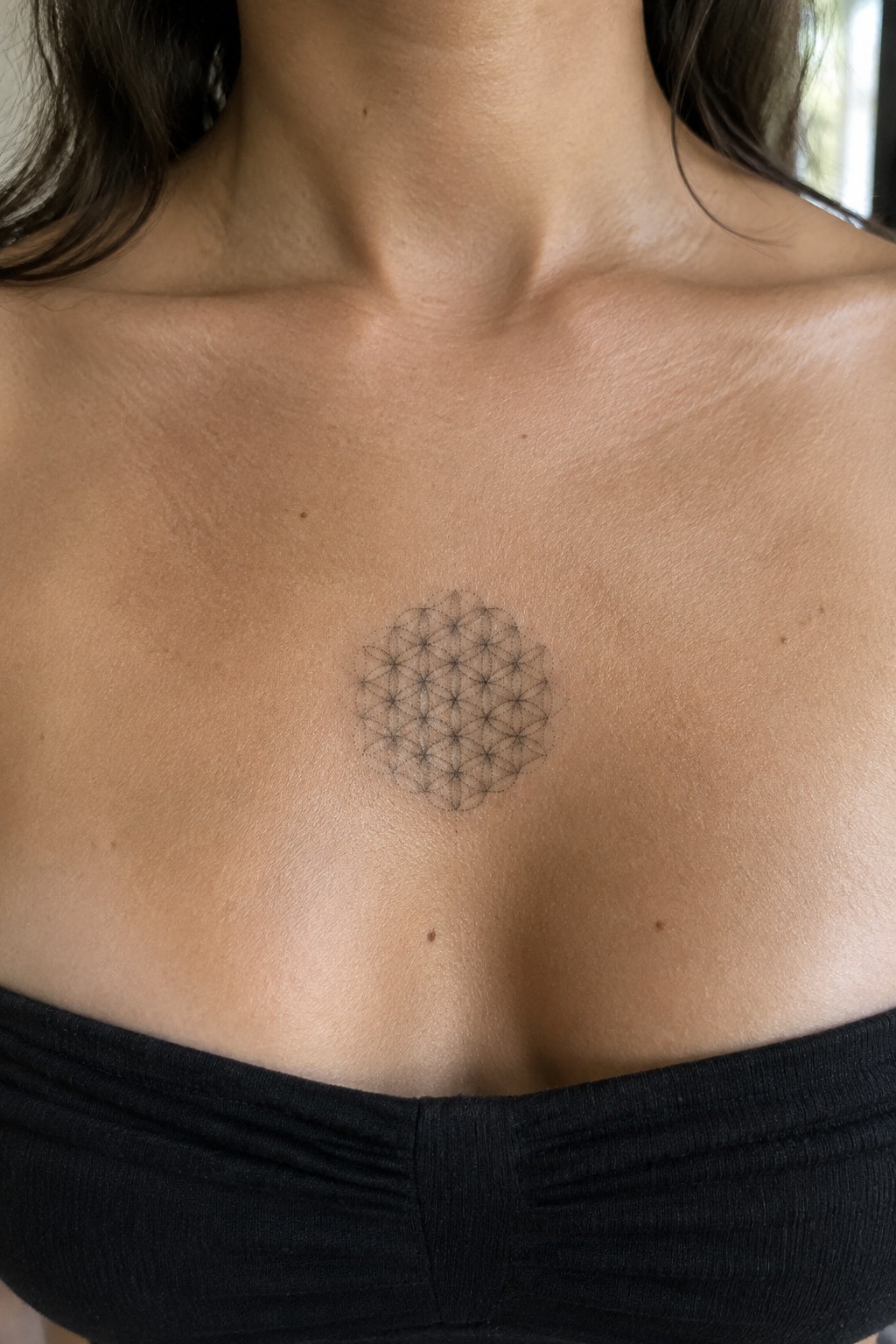 Circular geometric tattoo centered on light skin above black strapless top