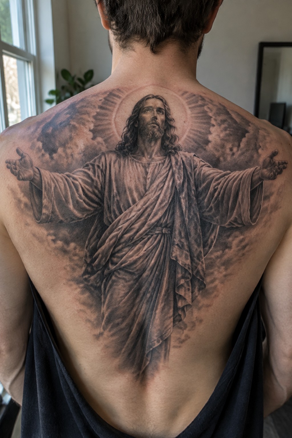 Large realistic tattoo of Jesus with outstretched arms amid clouds on man's back.