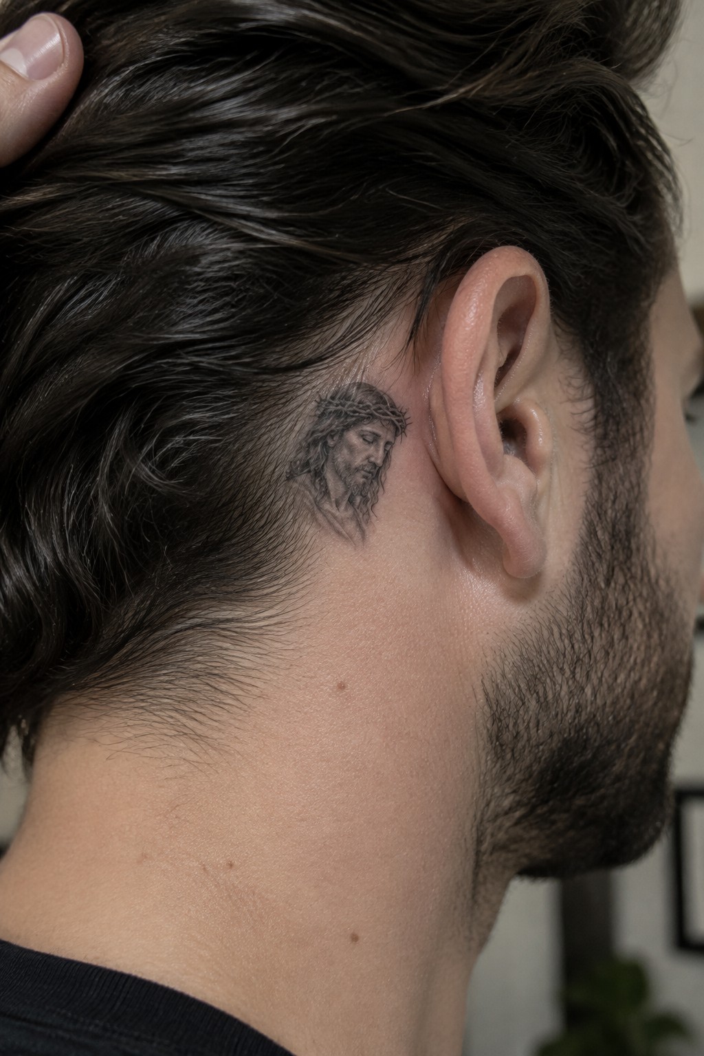 Bearded man with dark hair shows Jesus tattoo behind ear
