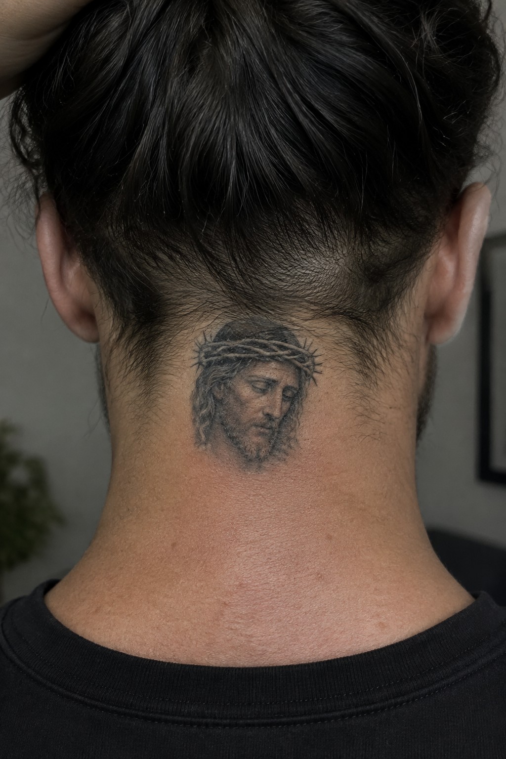 Dark-haired man in black shirt shows Jesus tattoo with crown of thorns on neck.
