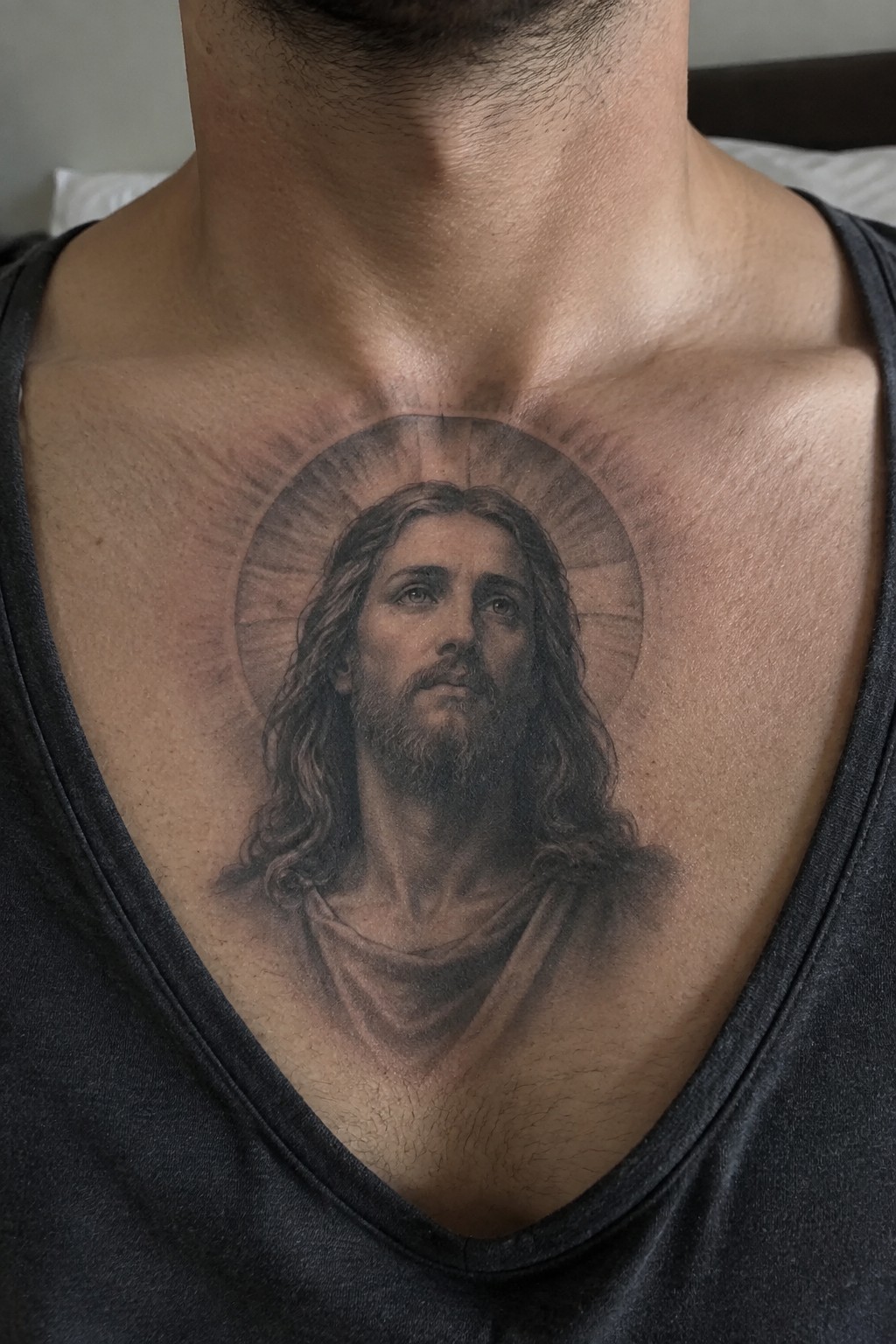 Realistic black-and-gray tattoo of Jesus with radiant halo on man's chest