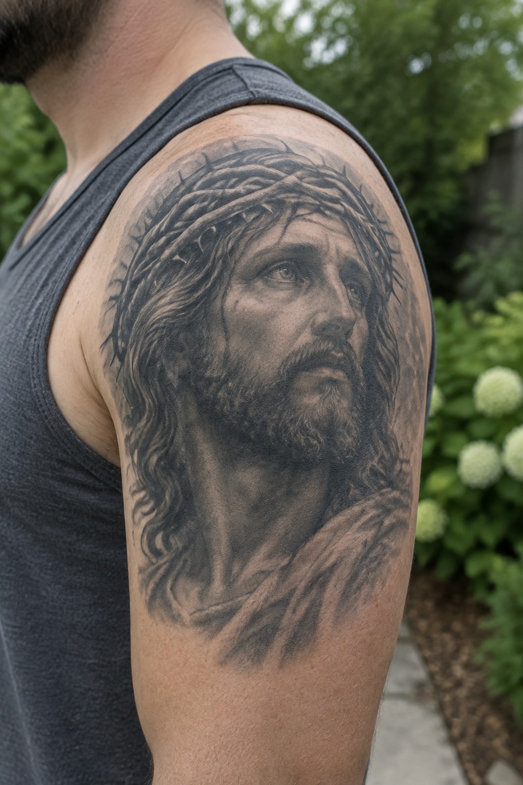 Man in gray tank top with detailed black-and-gray Jesus crown of thorns tattoo on shoulder