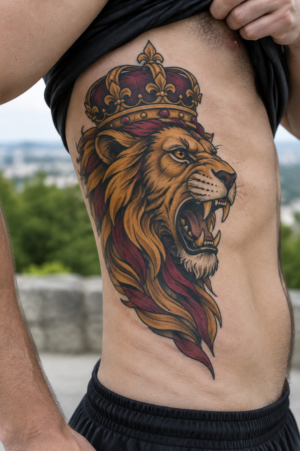 Neo-traditional tattoo of a roaring lion wearing a red and gold crown on a man's side torso