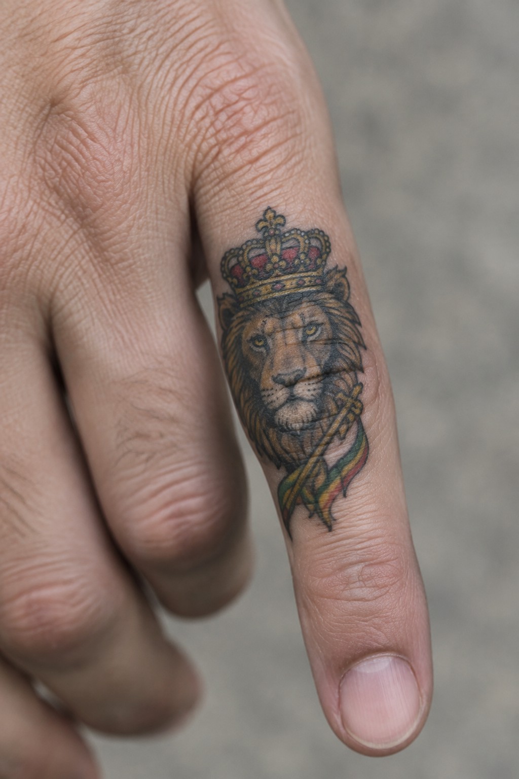 Crowned lion tattoo with scepter and colorful ribbon on a finger